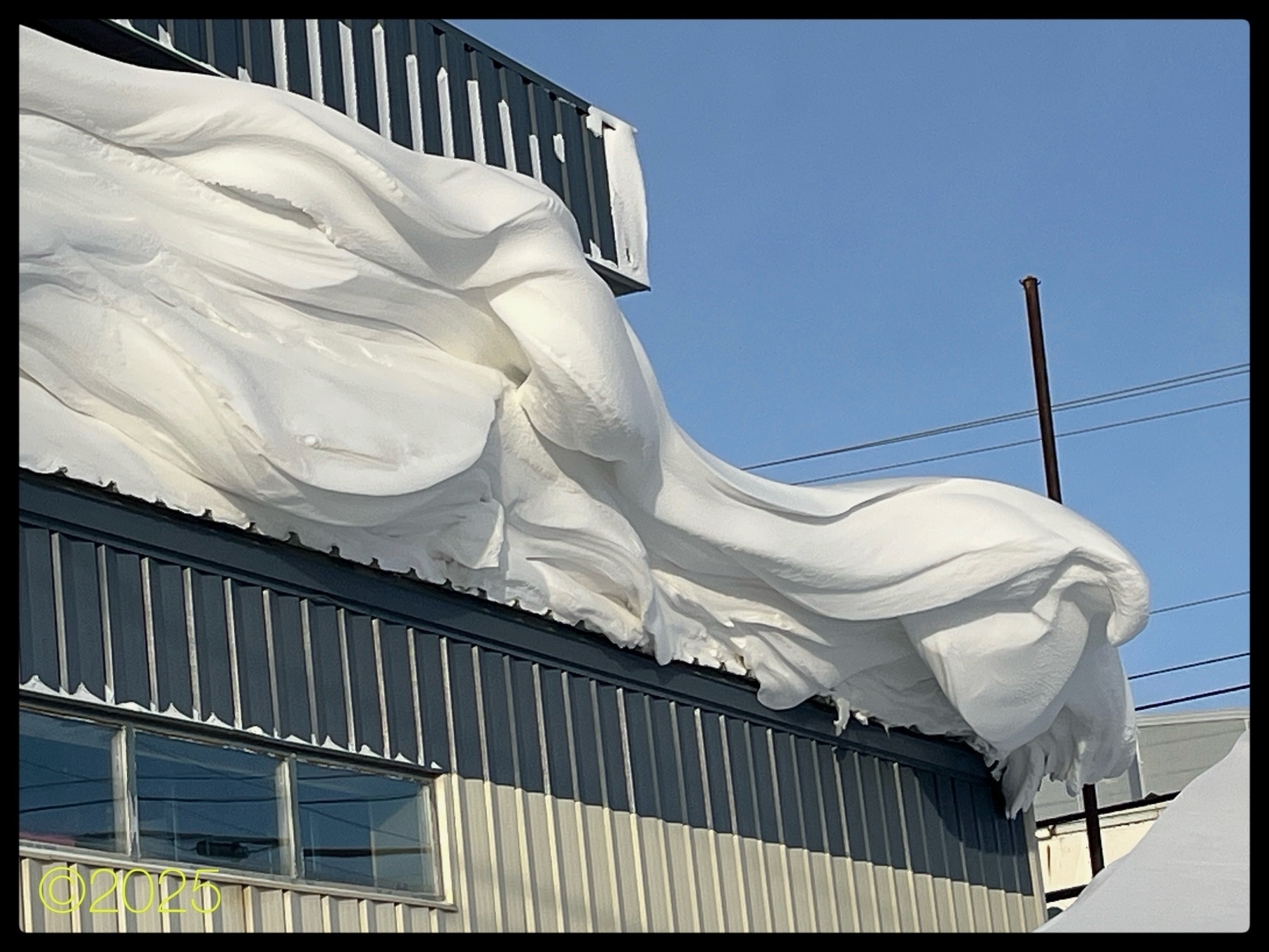 Large, sculpted snow formations hang over the edge of a building's roof, creating an impressive overhang.