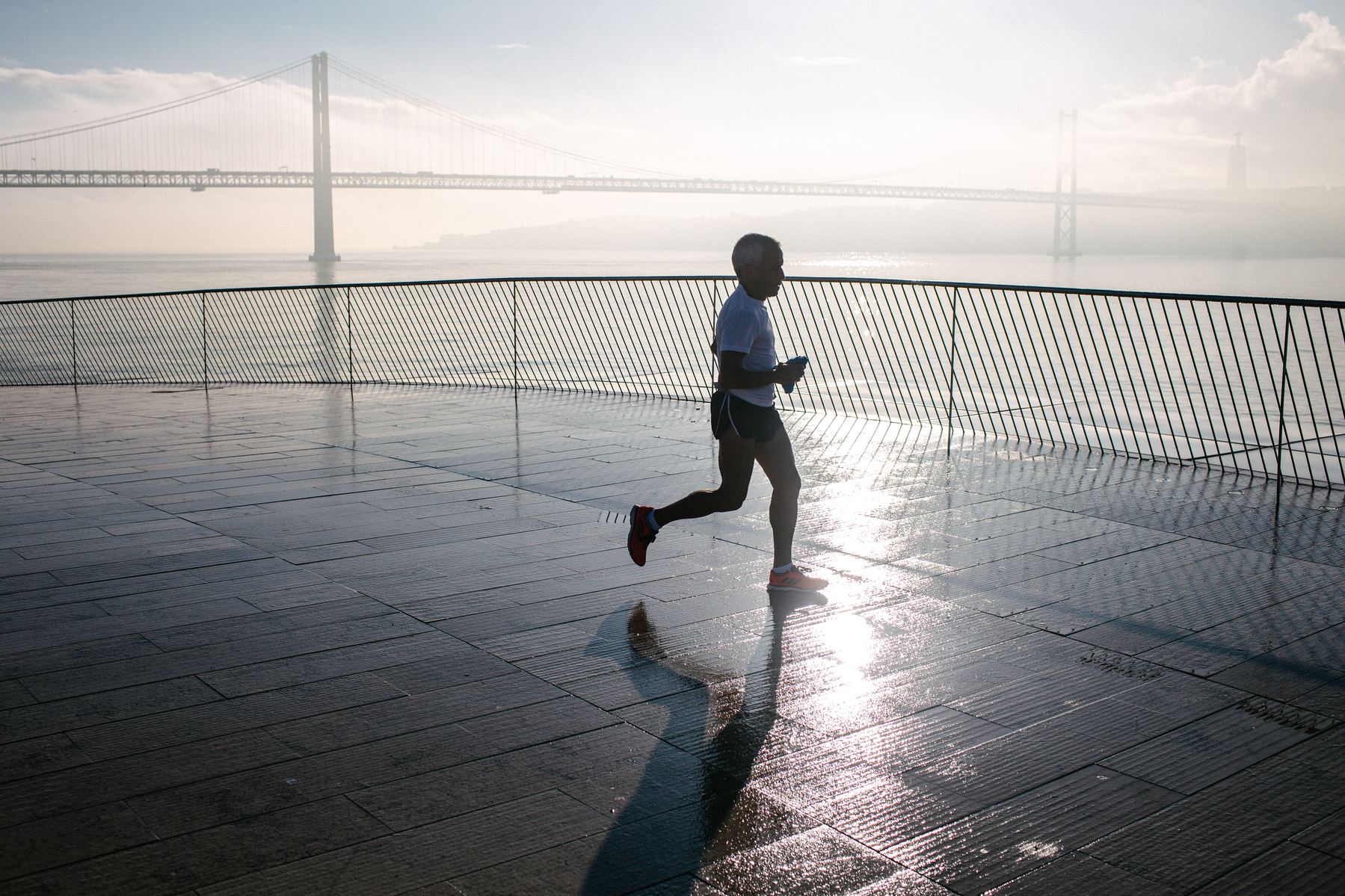 A man runs, with a river and a bridge in the back. 