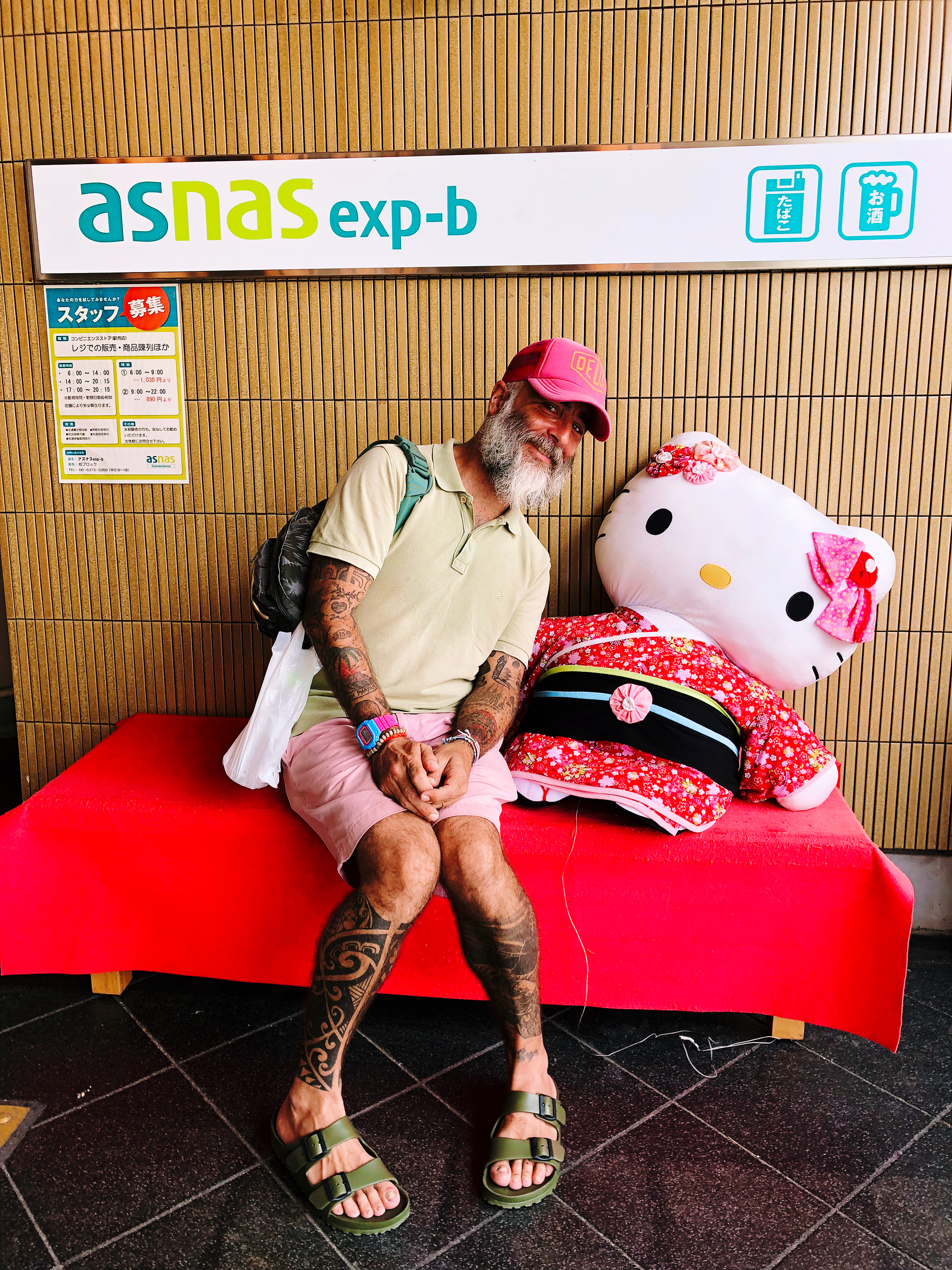 A man sits on a bench, smiling, with Hello Kitty, who’s wearing a kimono. 