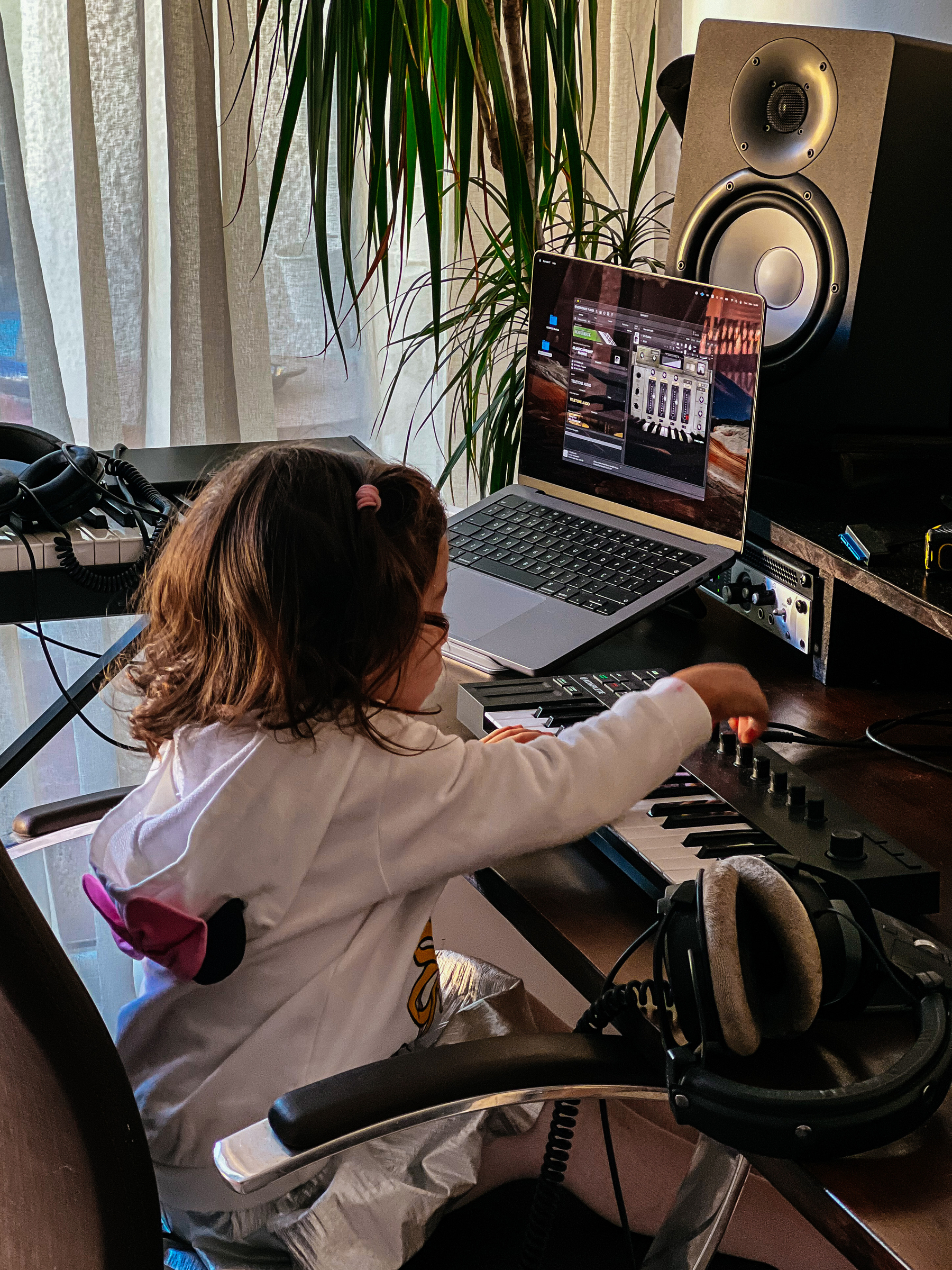 Toddler fiddling with a keyboard. Speakers, laptop, in front of her 