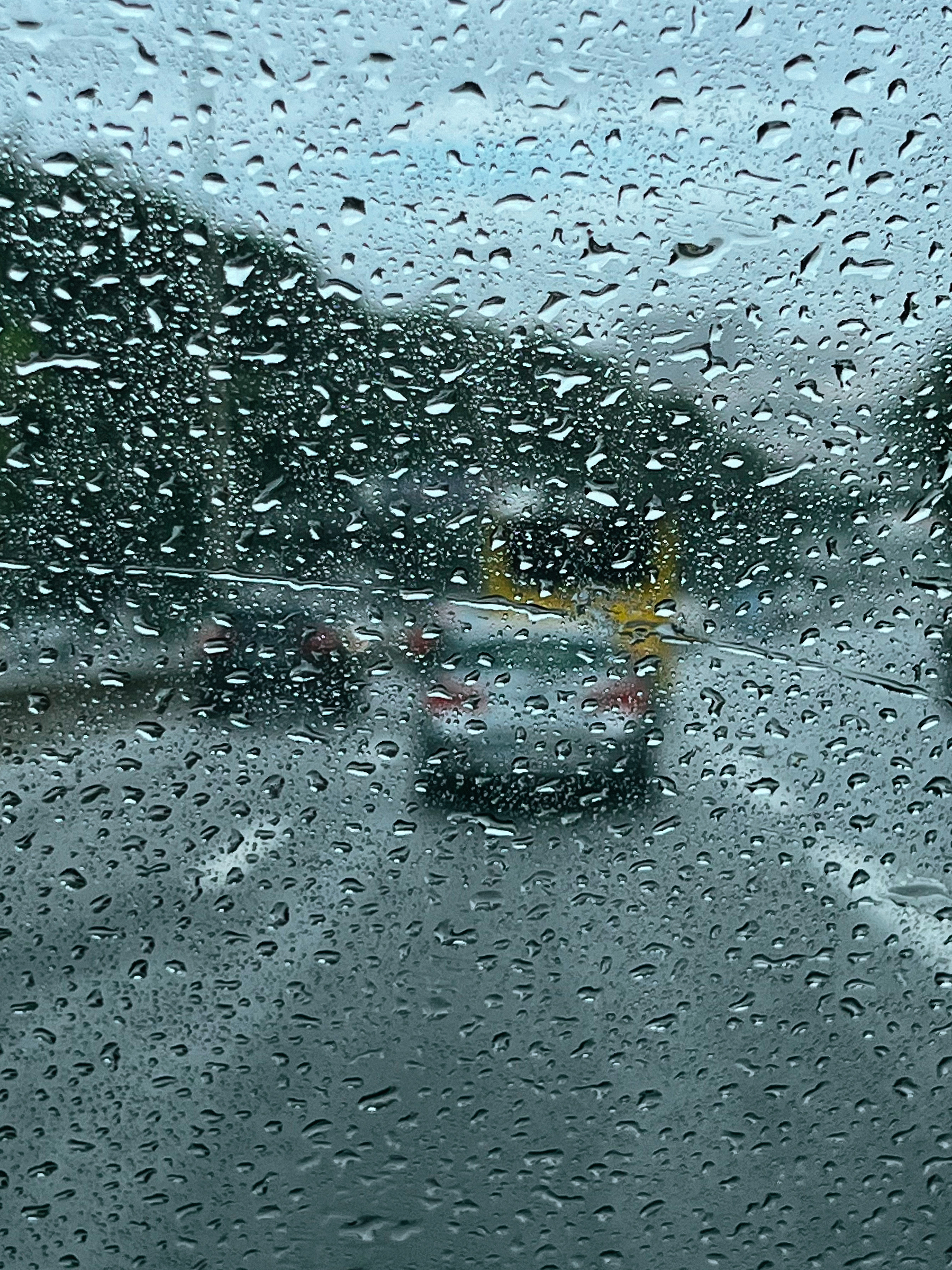Rain on a windshield, with the road in front of us. Highway, with cars. 