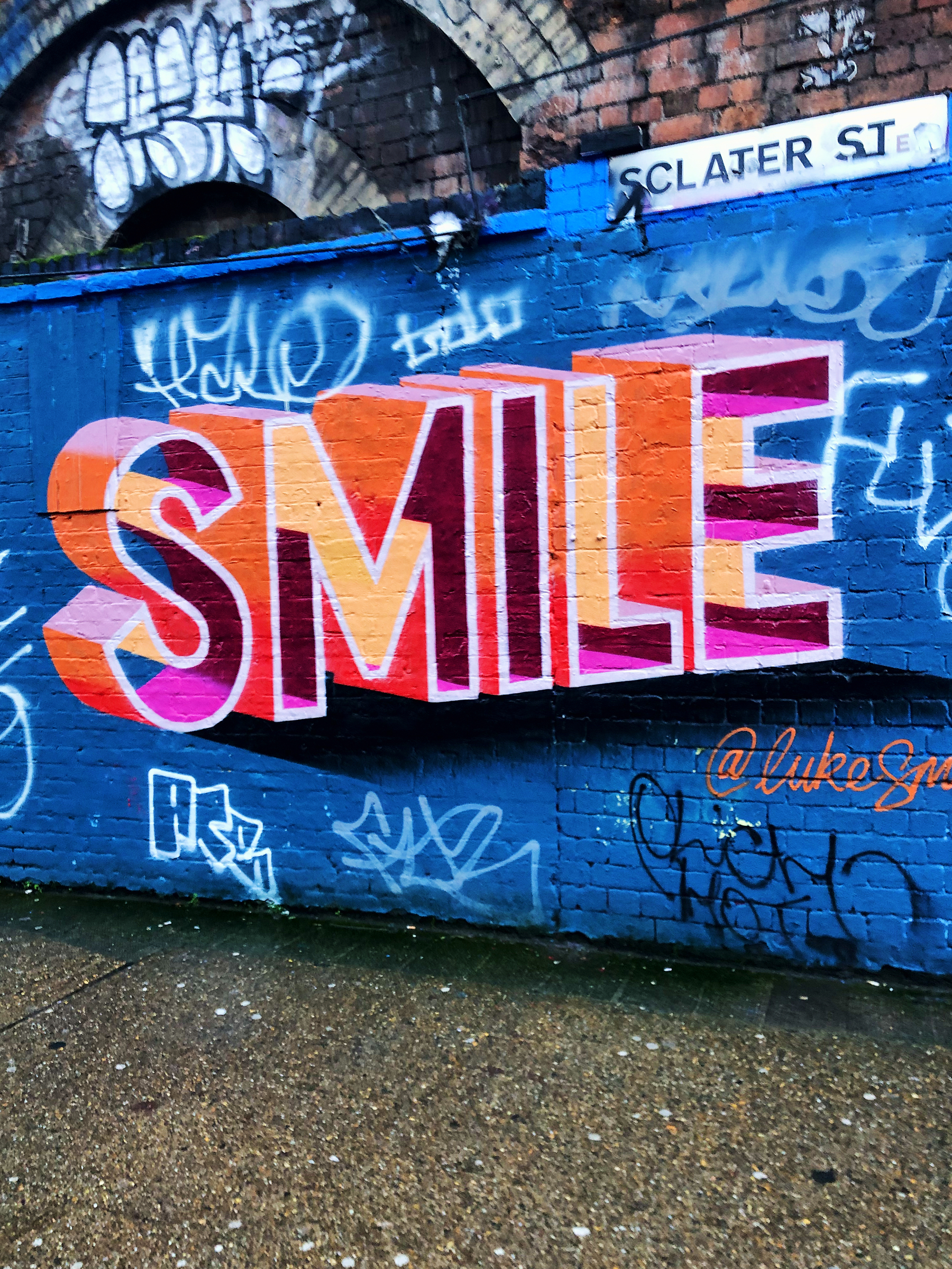 A blue wall with the word “Smile” written on it, in a lovely street art piece. 