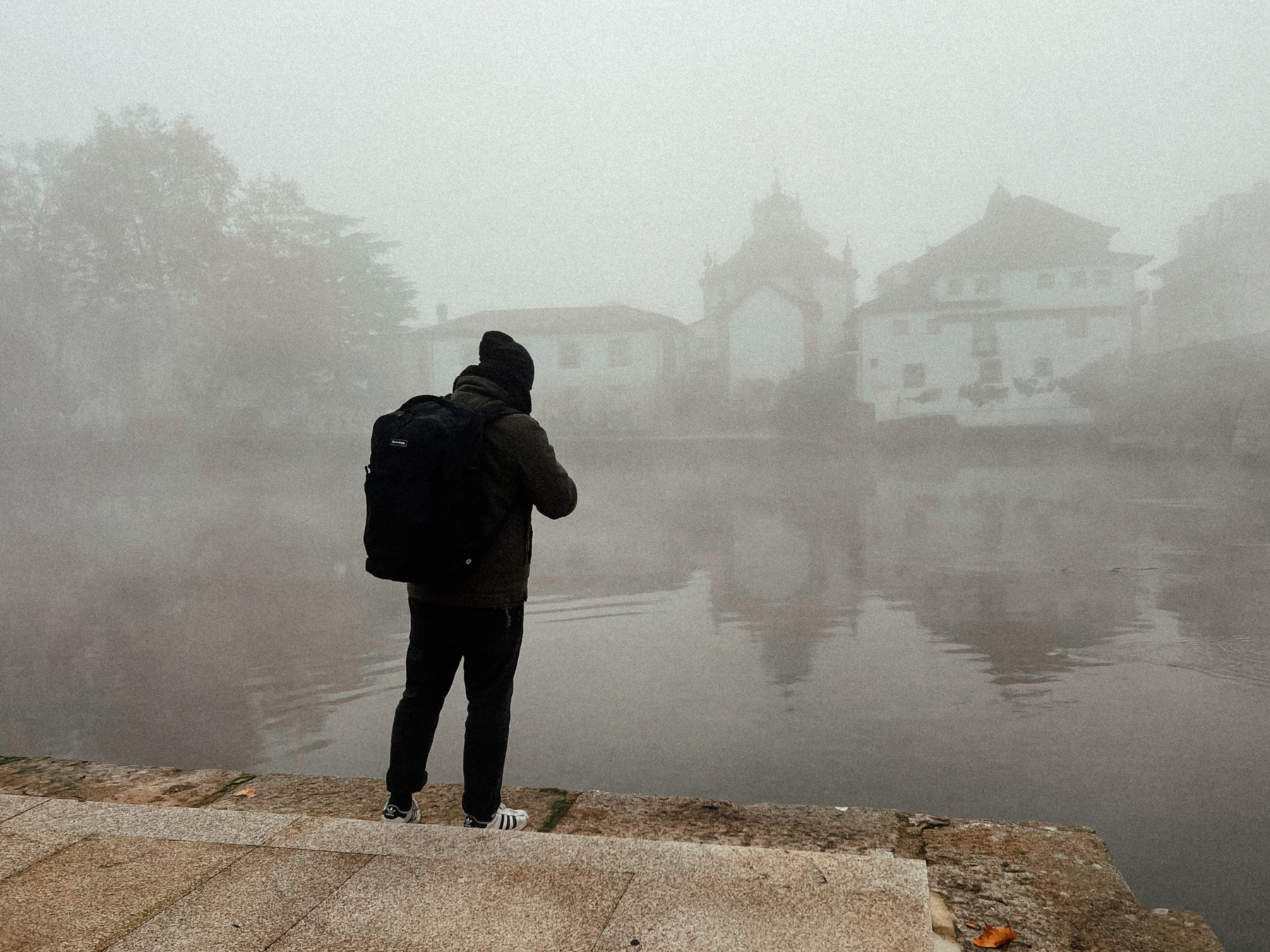A man takes a photo of a river in a misty morning. 