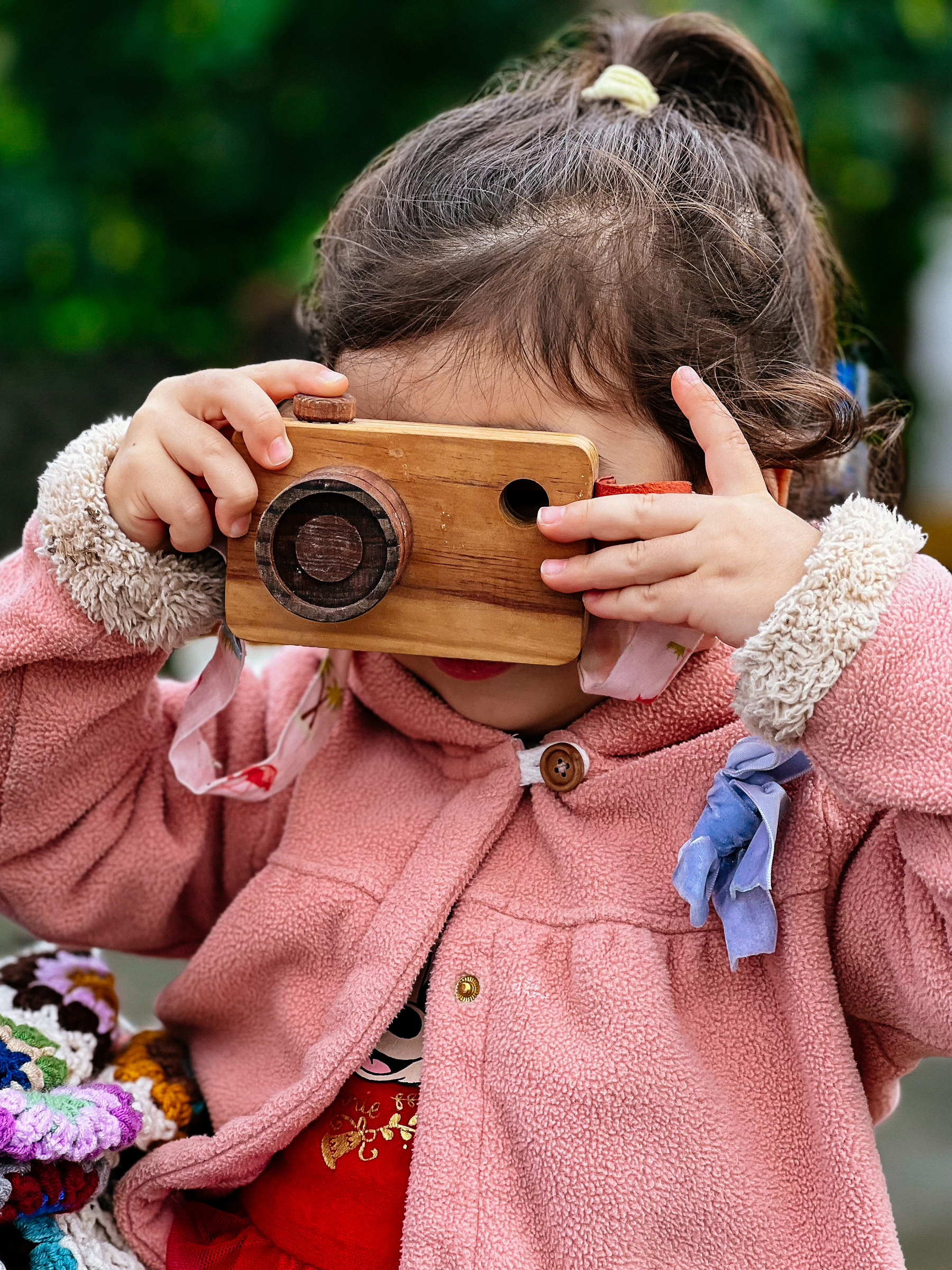 A little girl pretends to shoot with a wooden camera. 