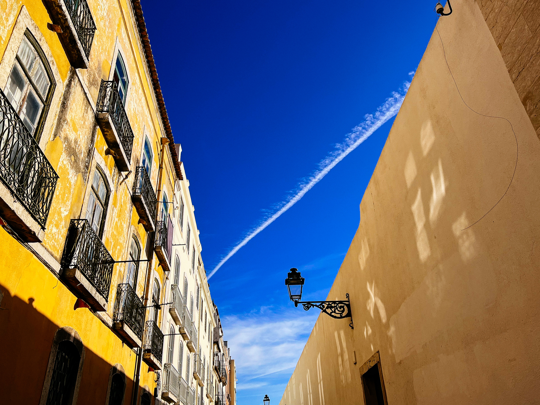 Looking up into the sky, the trailing cloud from an airplane crosses the sky, flanked by two buildings