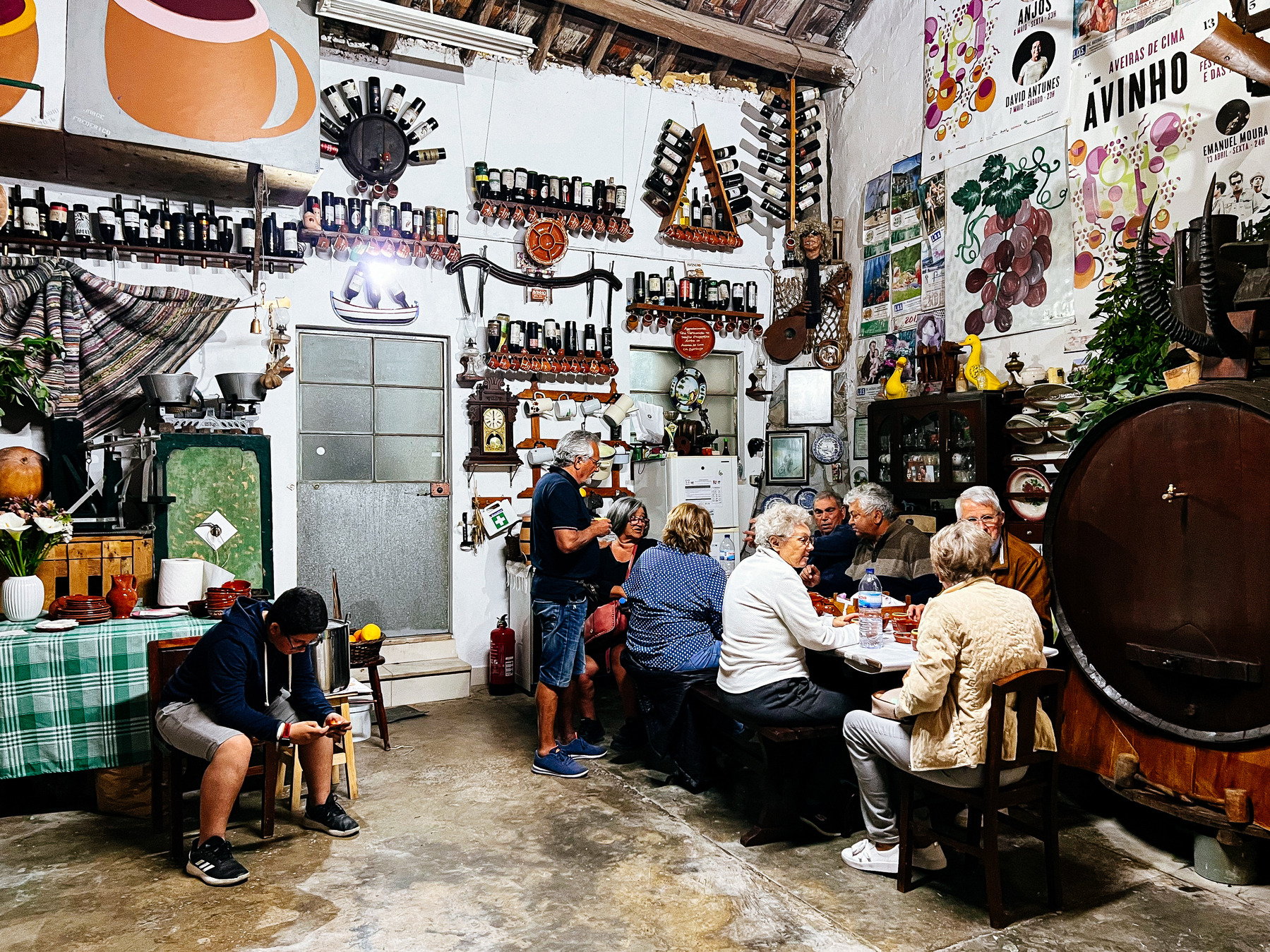People eat sitting at a table inside a wine cellar. The walls are covered with bottles and other wine-related memorabilia.