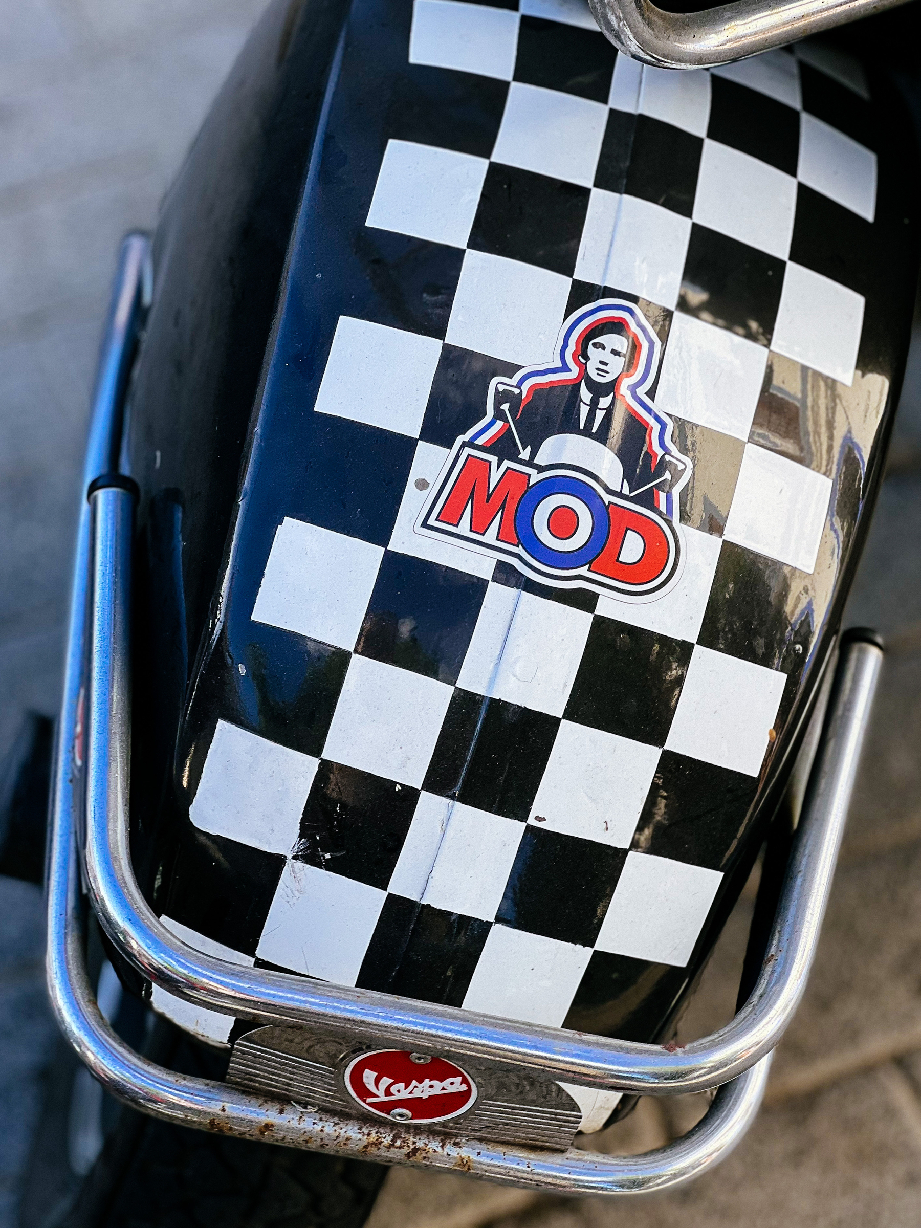 front wheel of a motorcycle, the word “mod” on top of a chess pattern