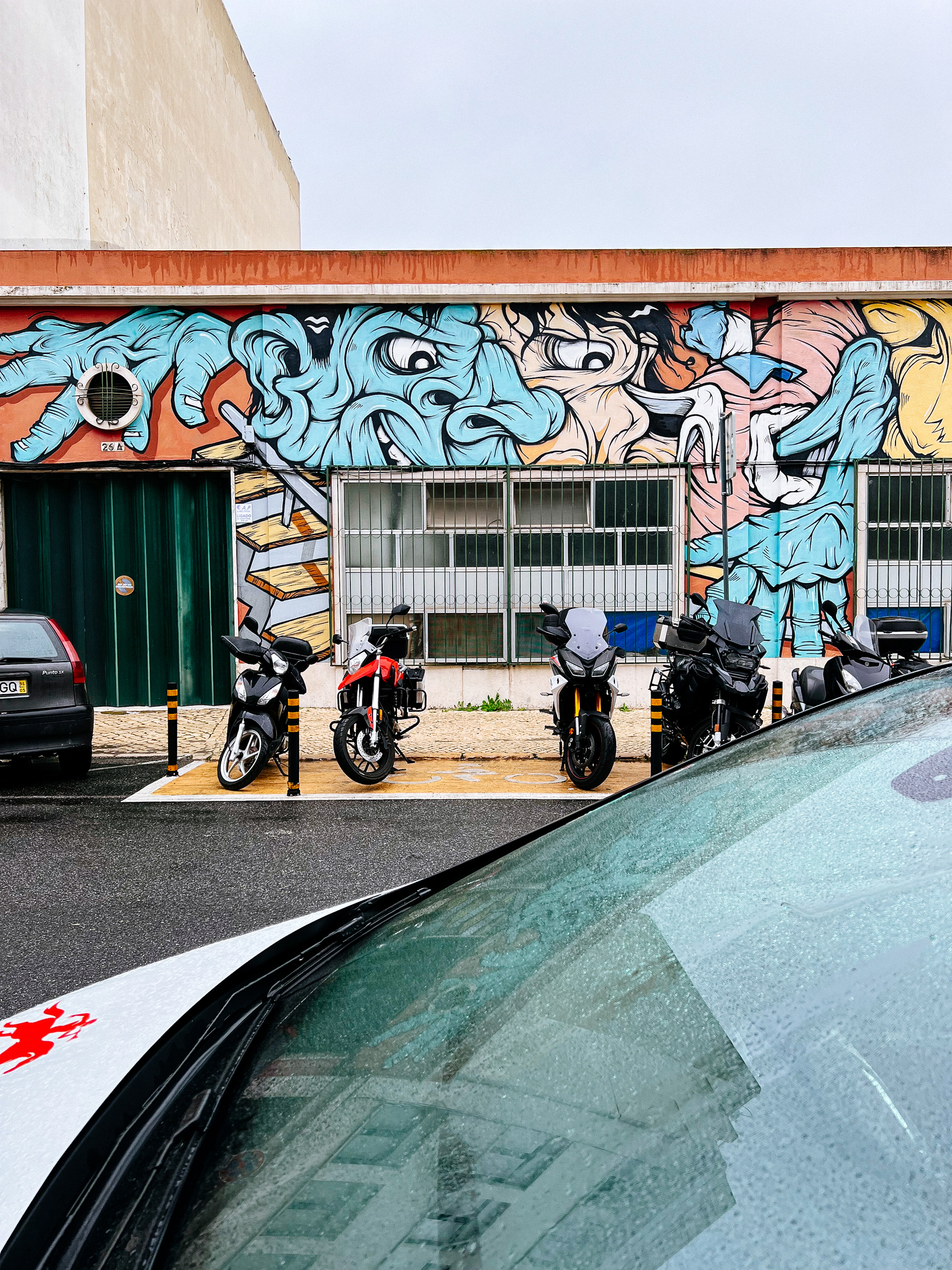 A few motorcycles are parked next to a building with some graffiti on the wall 
