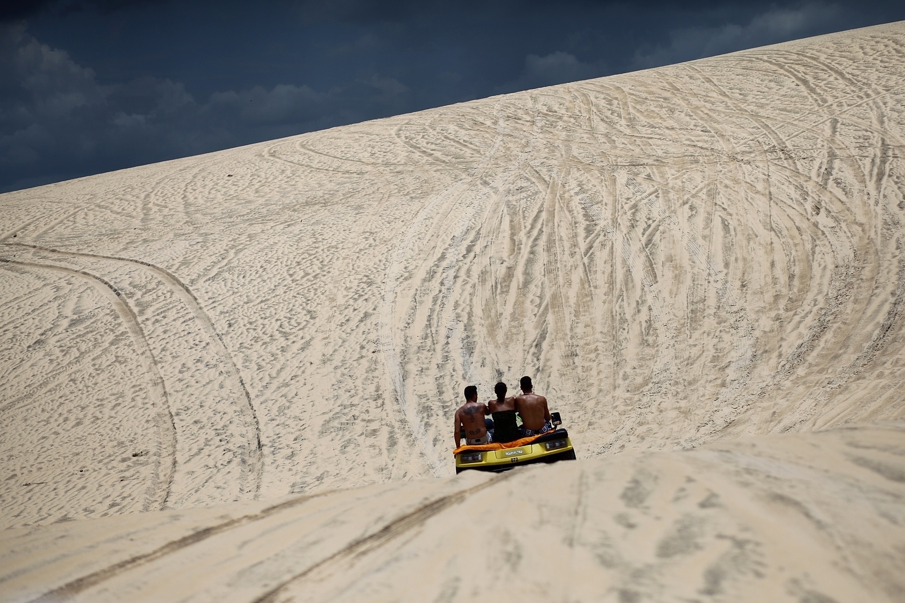 Three people sit on a buggy going down a dune.