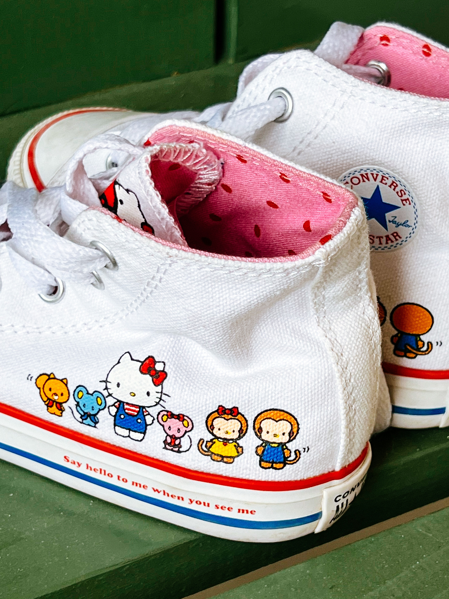 A pair of Hello Kitty themed sneakers sit on a bench. 