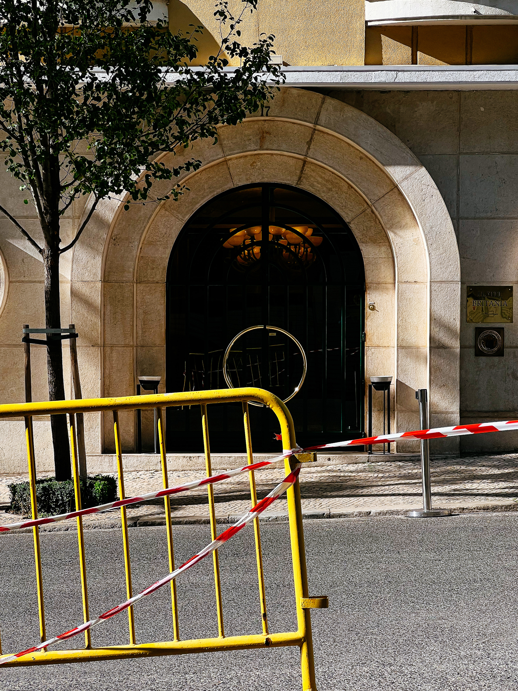 Entrance to a building, with an arch. On the foreground, a yellow fence