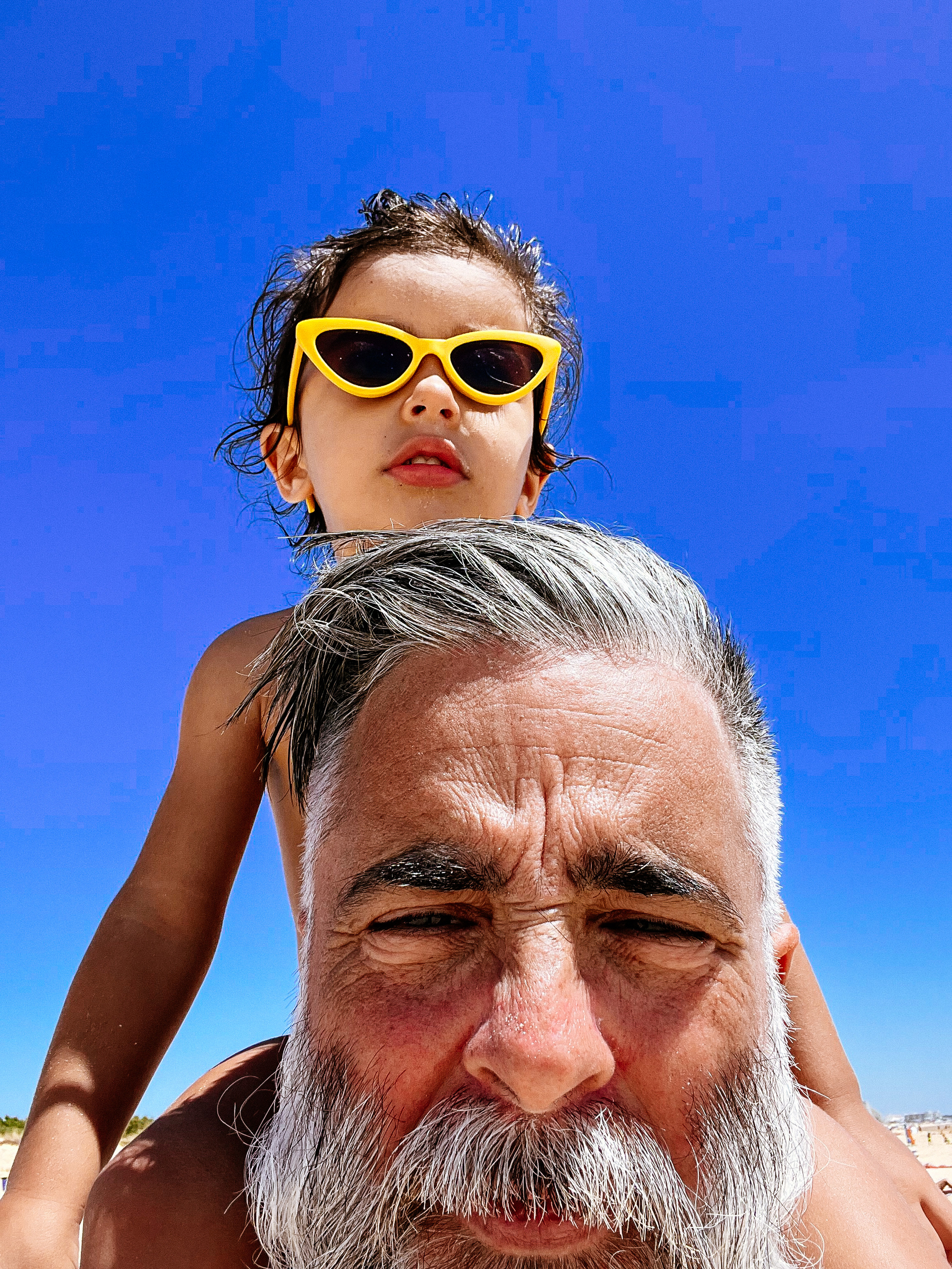 a toddler wearing yellow shades sits on daddy’s shoulders