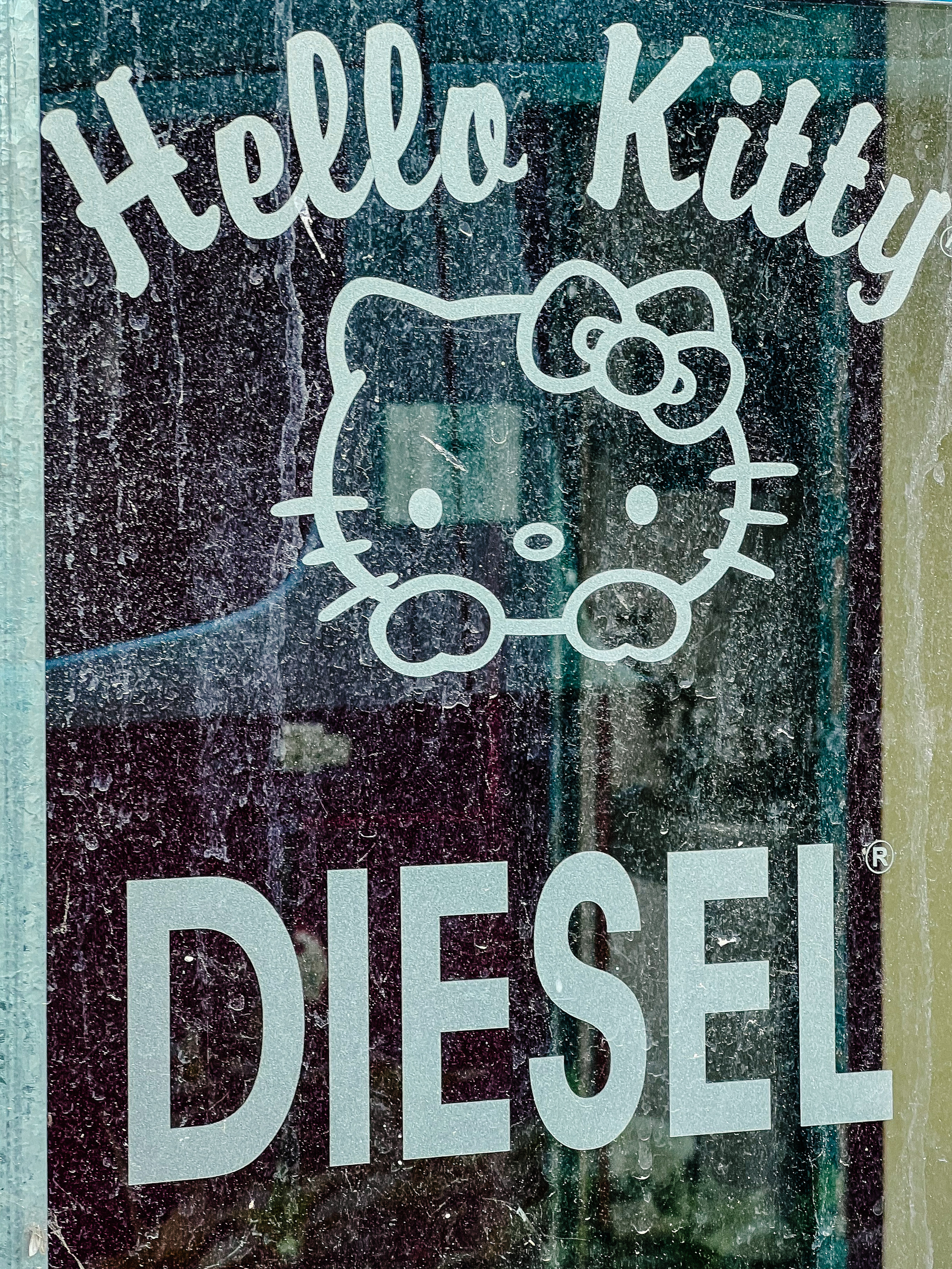 A very dirty window with a sticker of Hello Kitty, her name on top, and “DIESEL” below. 