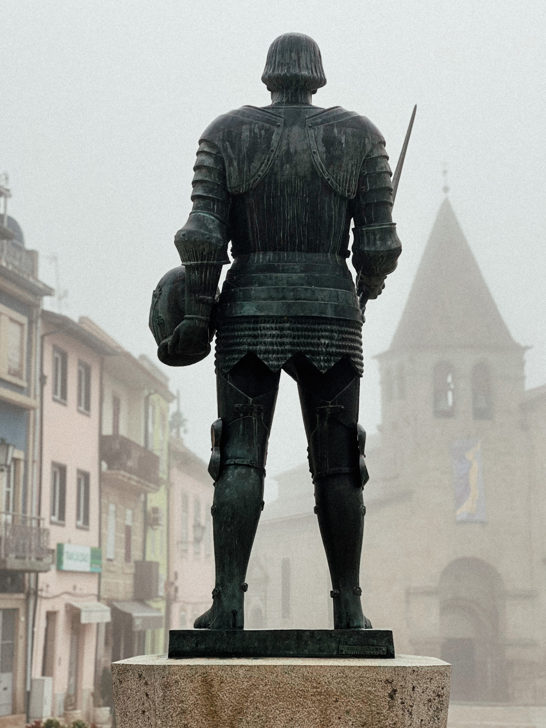 A statue stands in the middle of a square in the old part of town. 