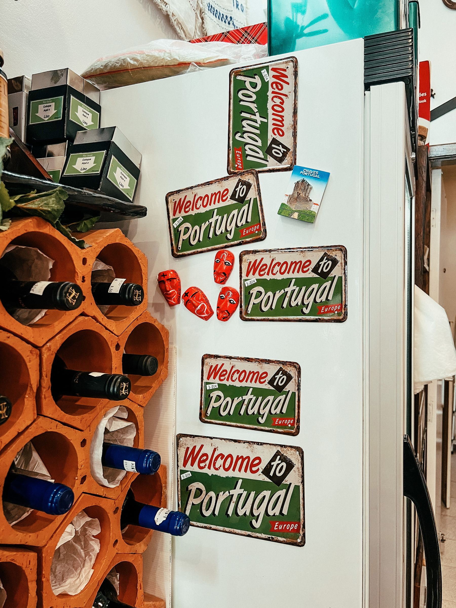 Bottles and a fridge. The fridge has magnets with the words “Welcome to Portugal”. 