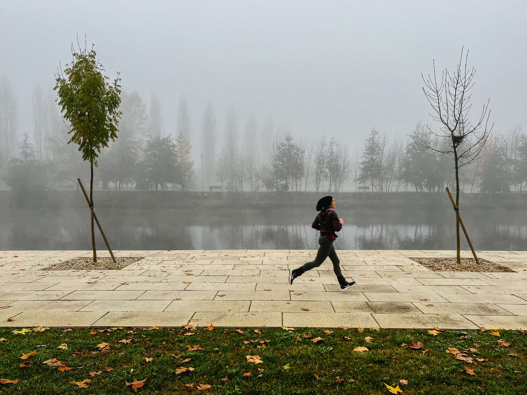 A woman runs close to a river, misty morning. 