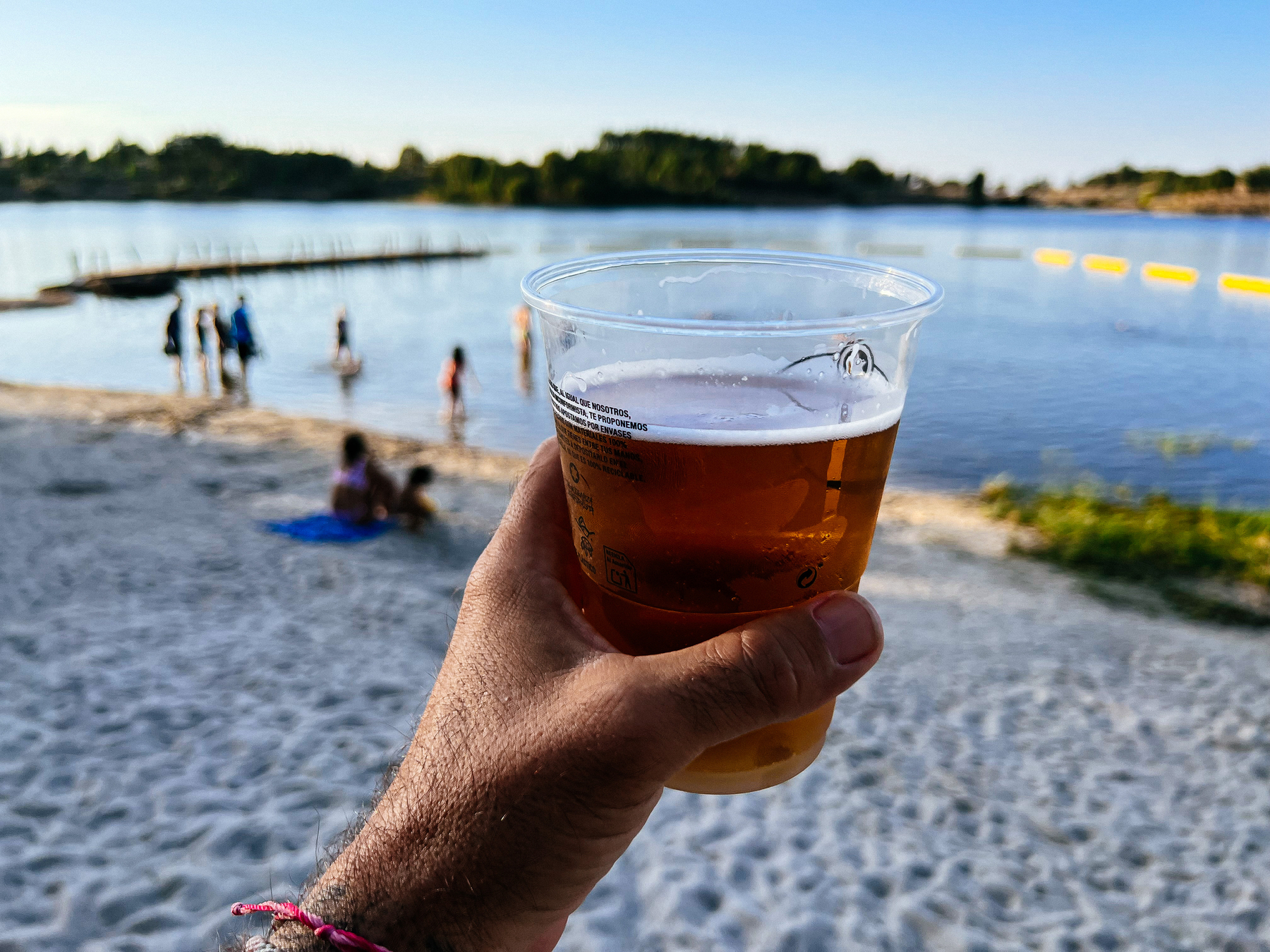 A hand holding a beer, next to a lake