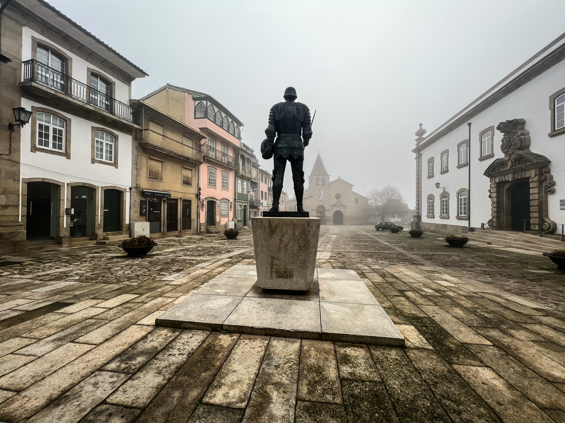 A statue stands in the middle of a square in the old part of town. 