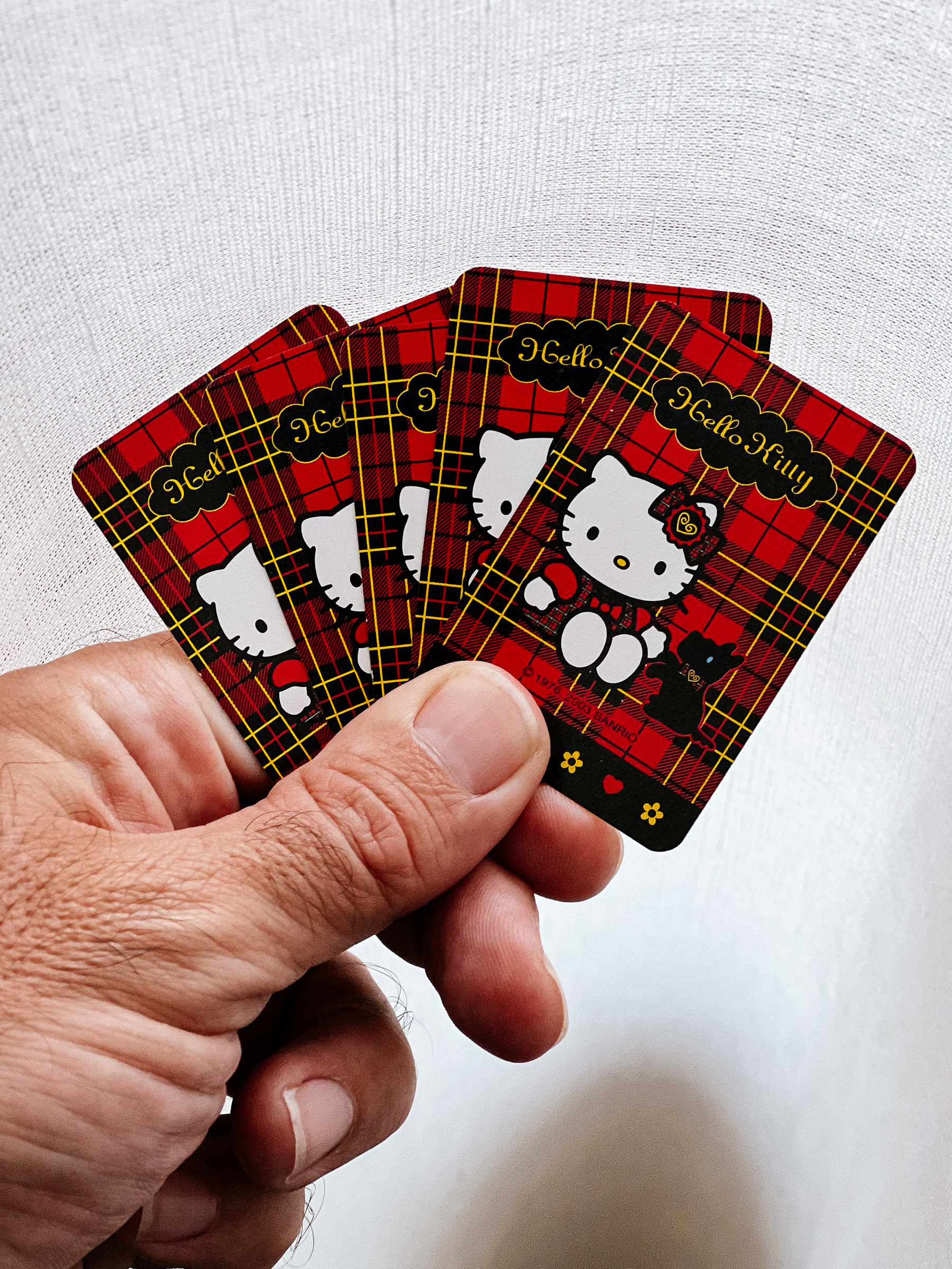 a hand holding five playing cards, with a Hello Kitty design in the back