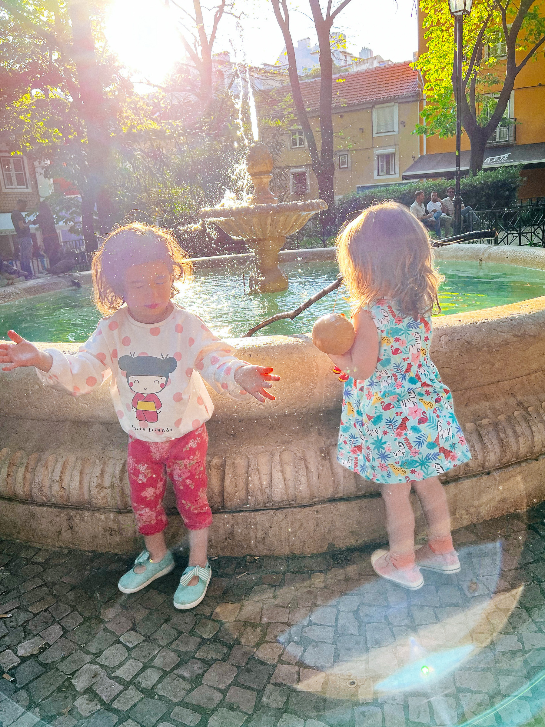 Two toddlers play by a water fountain. 