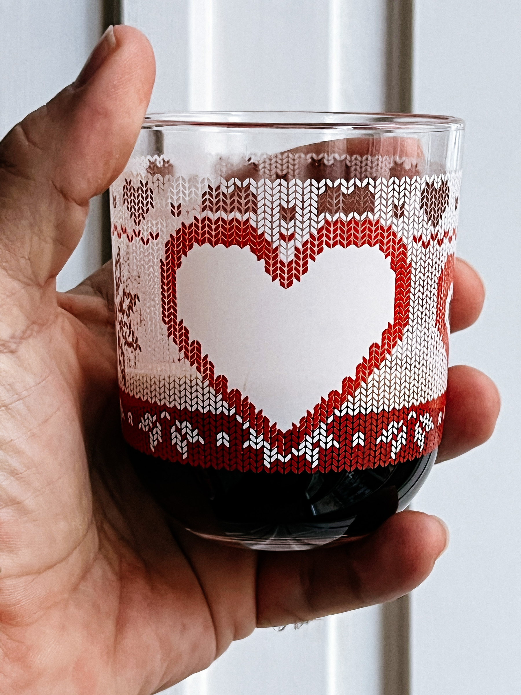 A hand holding a cup of coffee. The cup has a Christmas vibe, with hearts. 