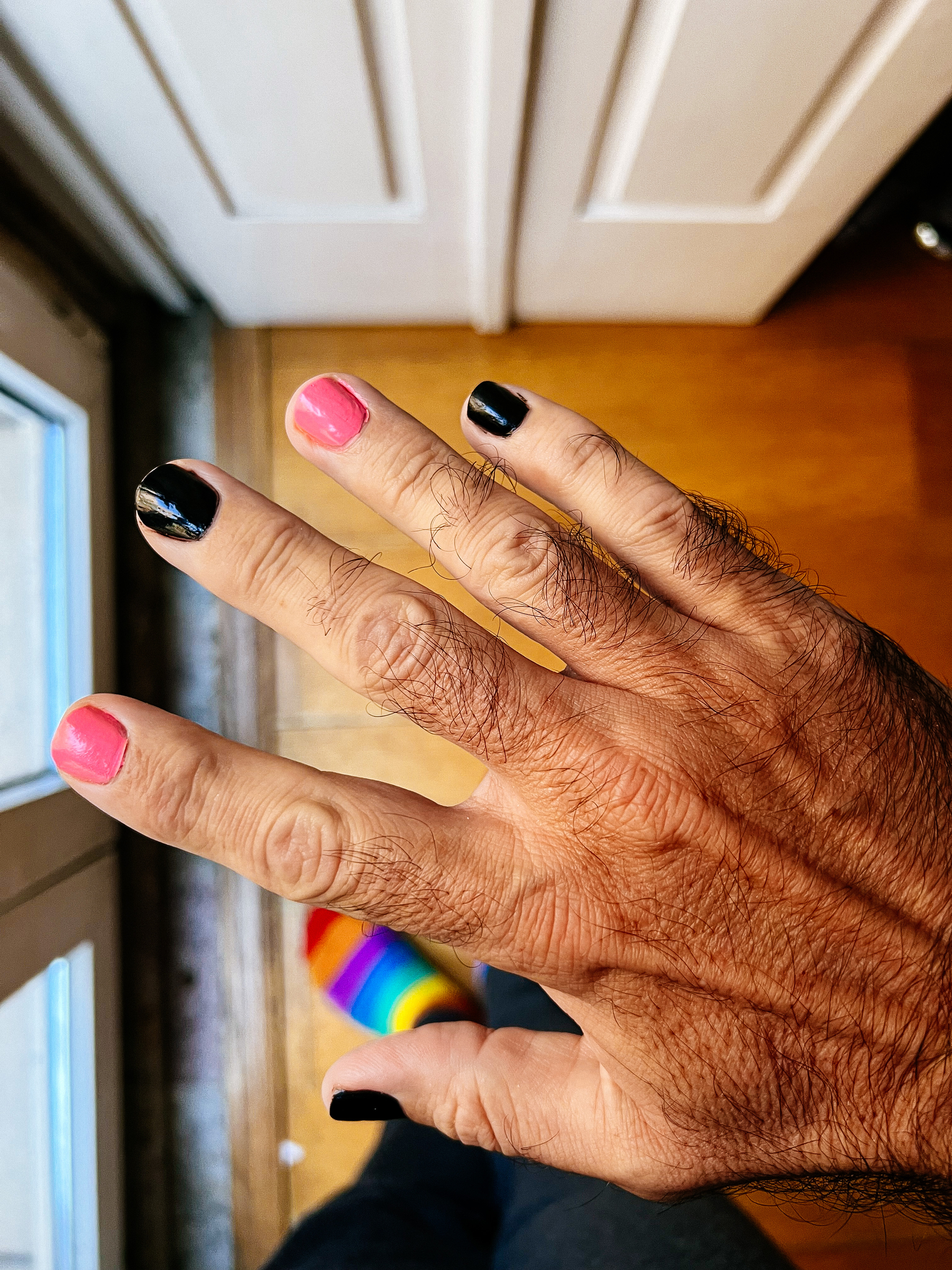 Looking down on a hand, nails painted in black and pink, on alternating fingers. 