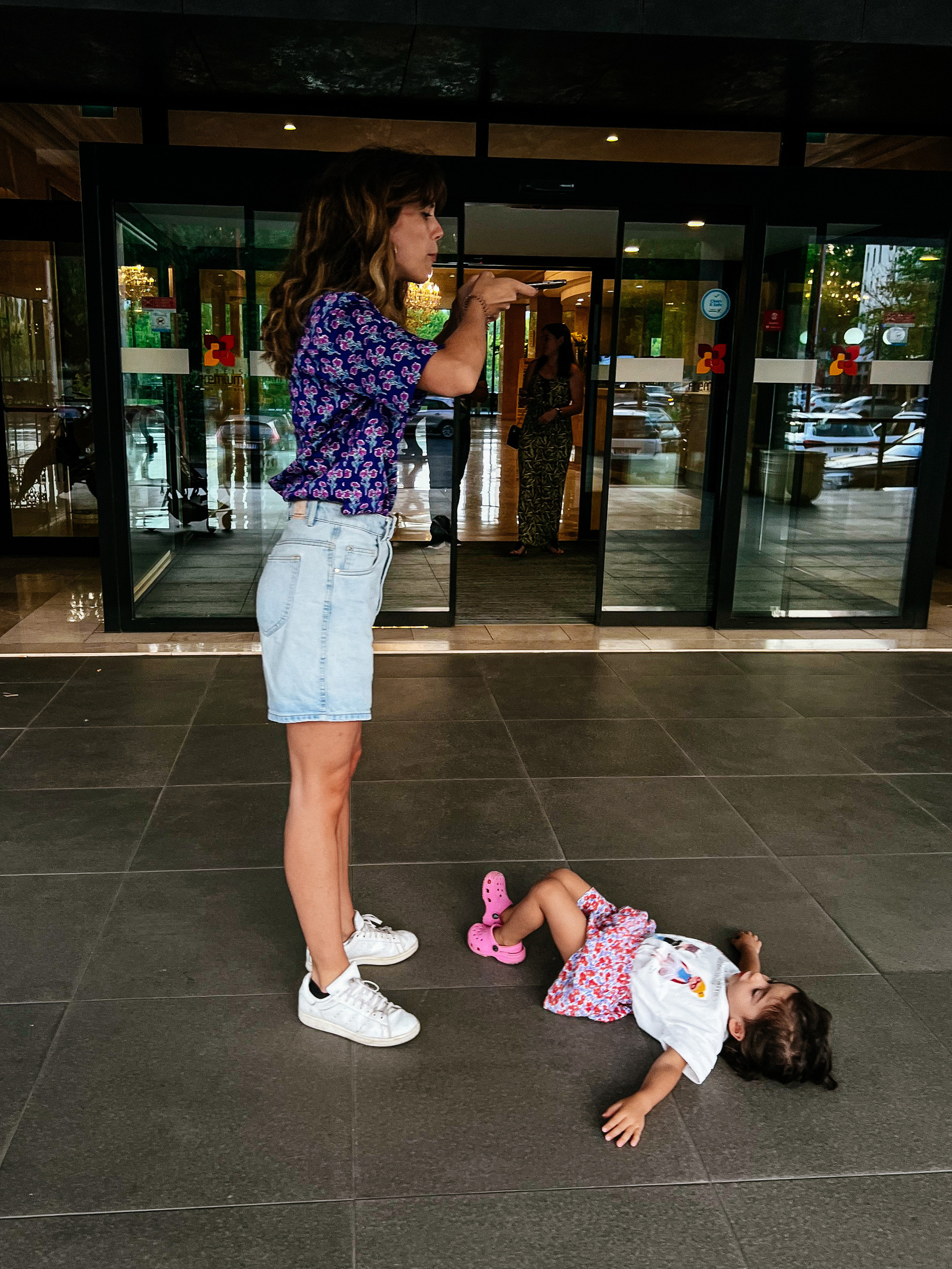 A girls takes a photo of a toddler who’s lying down on the floor 