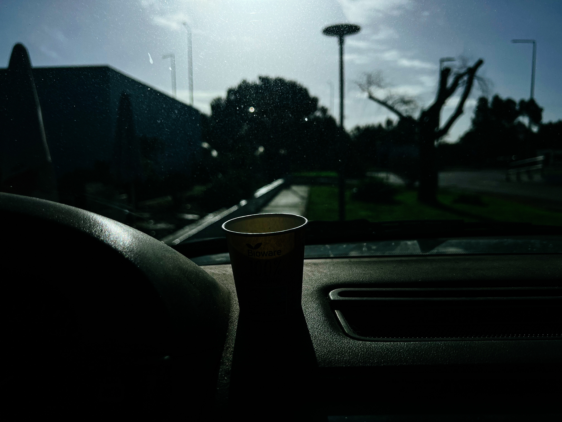 A lone coffee paper cup sits on a car dashboard. 