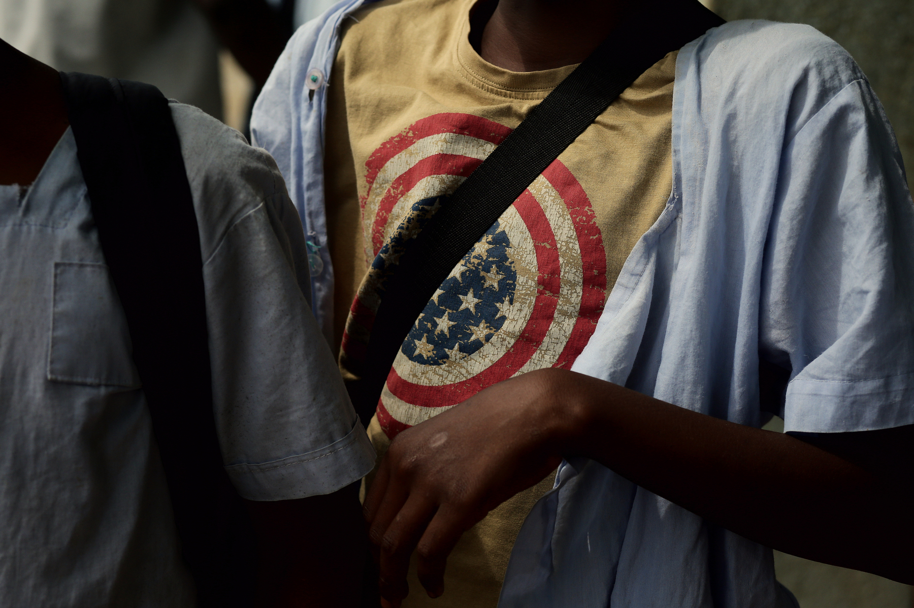 A school boy wearing a battered t-shirt with an American flag printed on it.