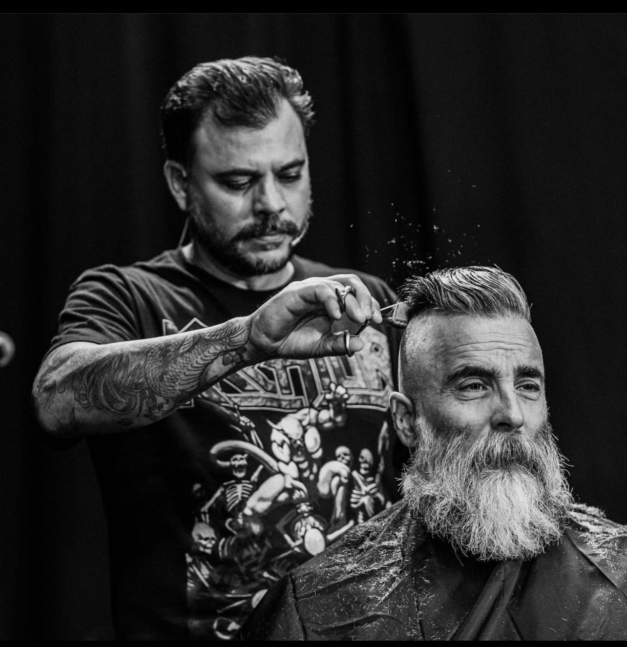A barber works on a bearded man. Black and white photo. 