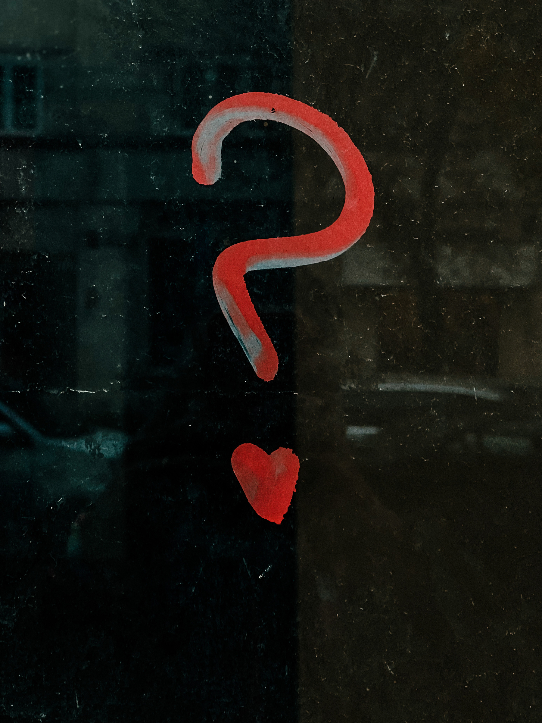 Graffiti of a question mark on a window, the dot on the question mark is a heart. 