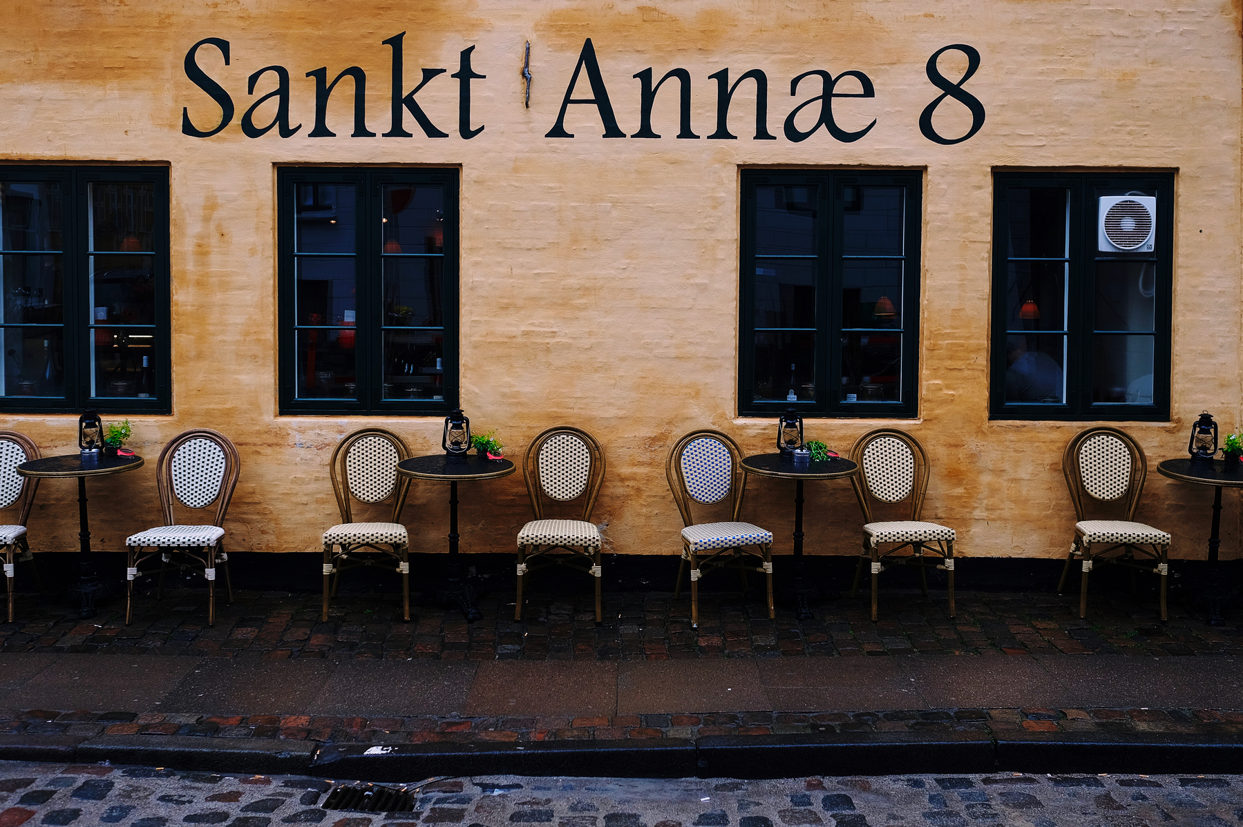 A row of chairs, neatly arranged against a wall. “Sankt Annæ 8” written on the wall. 