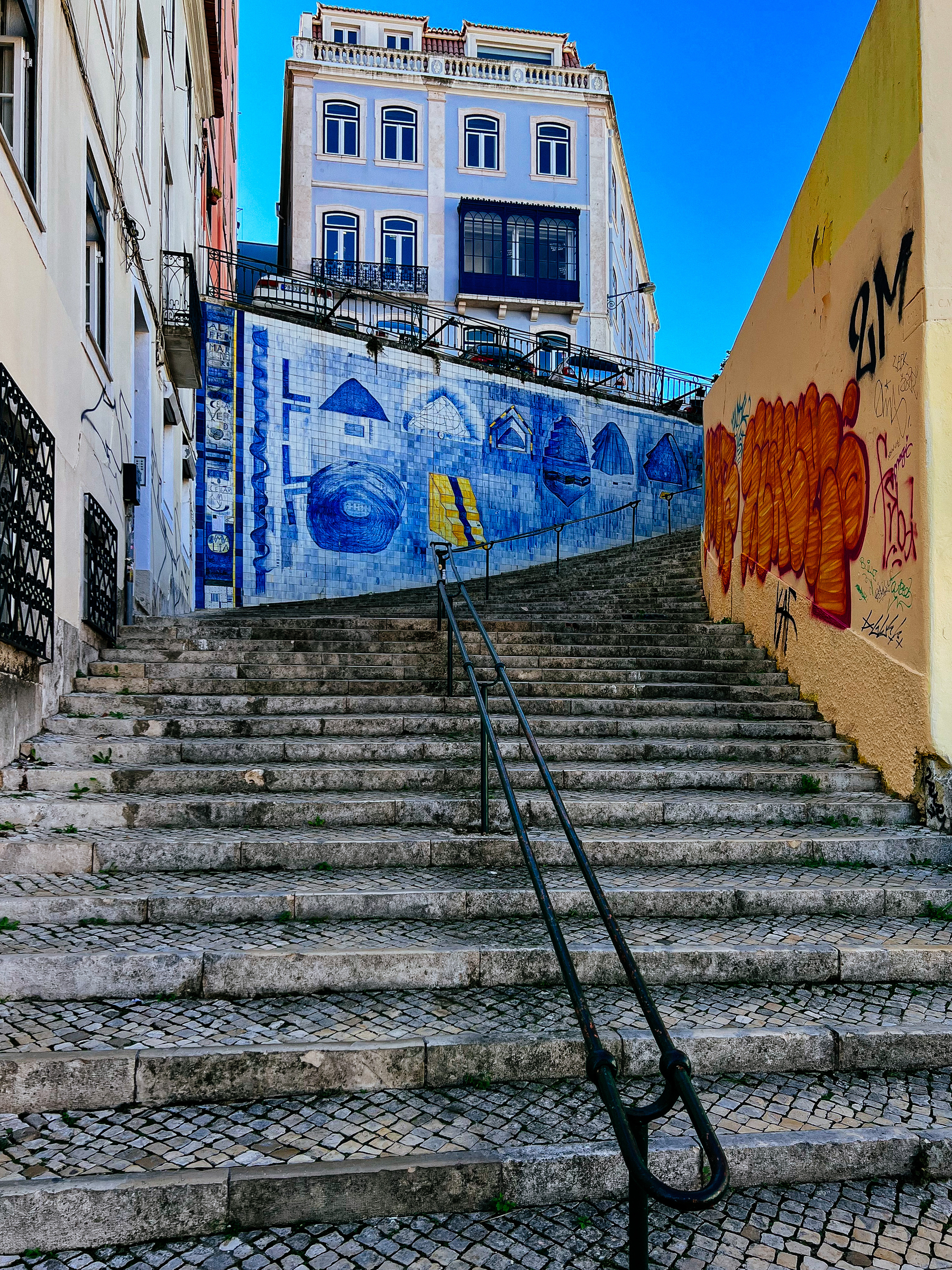 A stairway leading up to a tile panel, with a blue building higher up, on the background 