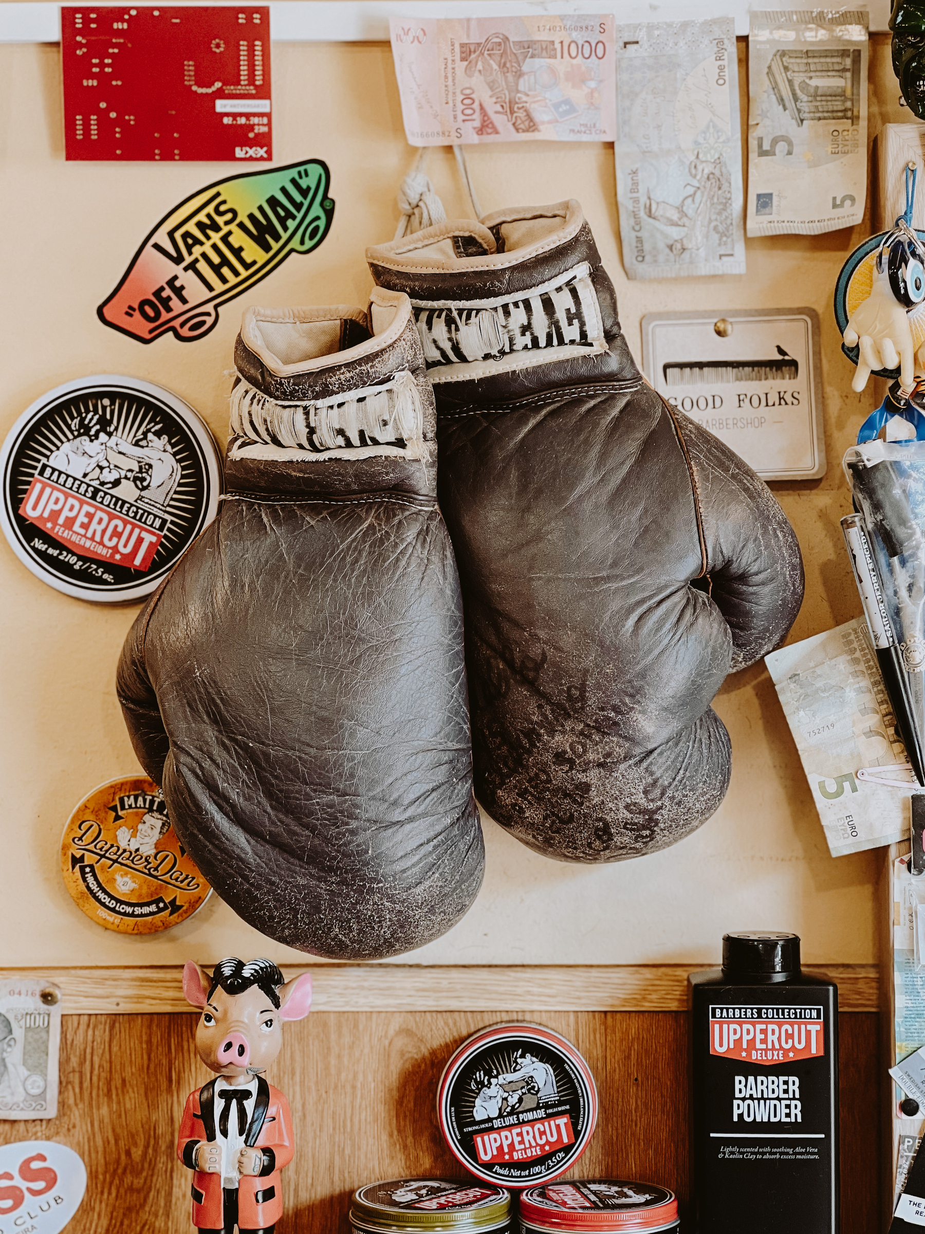 A pair of boxing gloves on a wall. Stickers and barber stuff around them. 