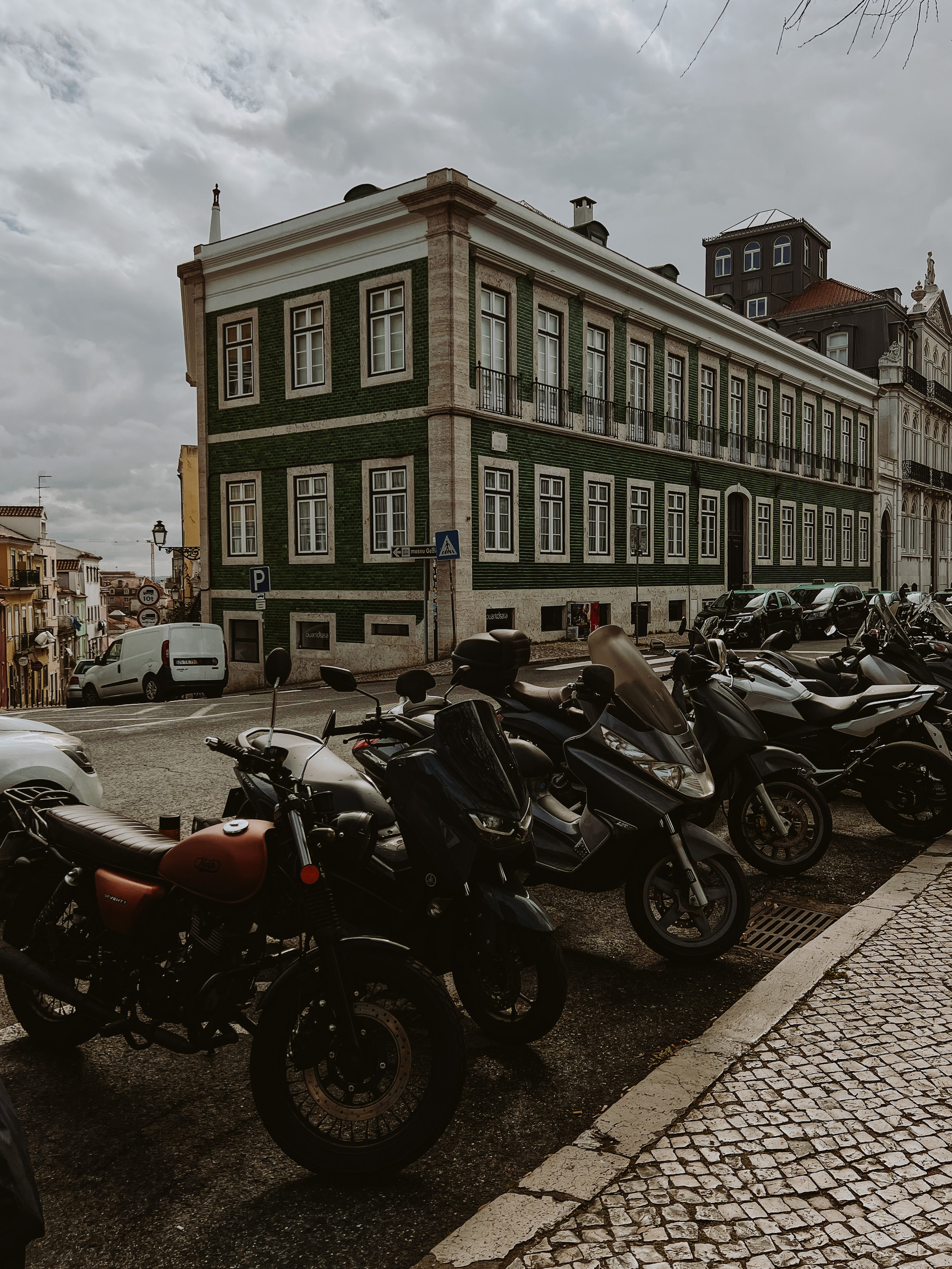 City view, with a building in the back, and a few parked motorcycles in the foreground. Darkish skies. 