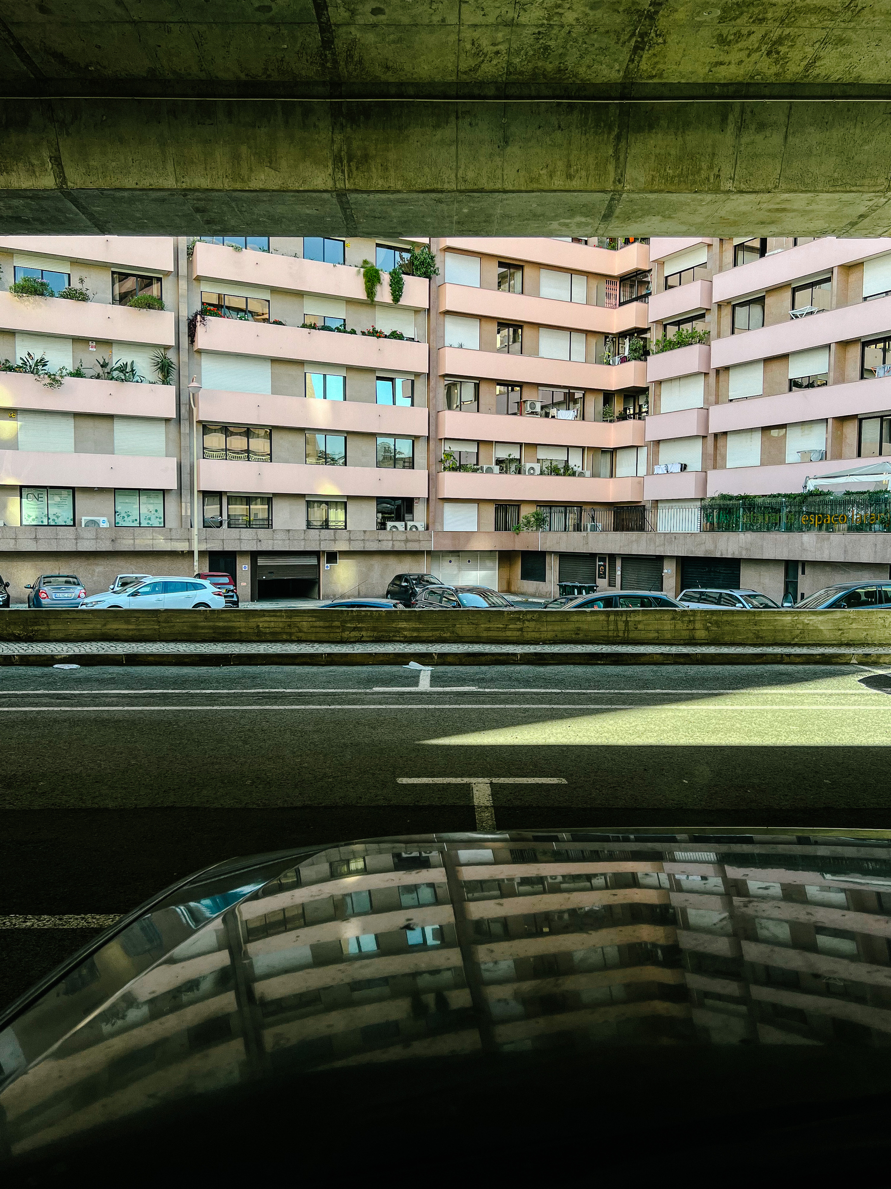 A pink building is seen from an underpass. It’s also reflected on the hood of the car from where the photo was taken. 