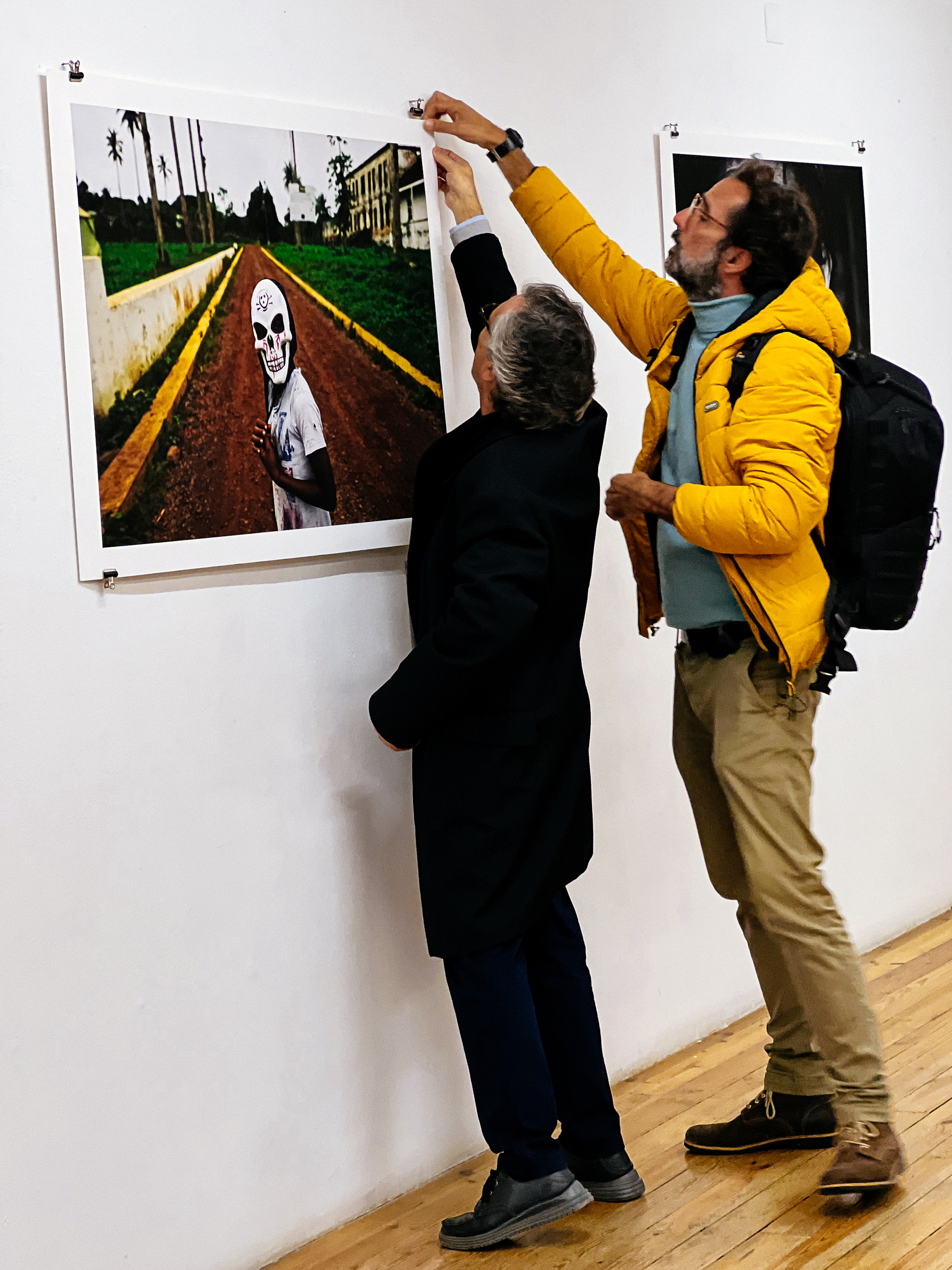 Two men hang a photo on a wall.