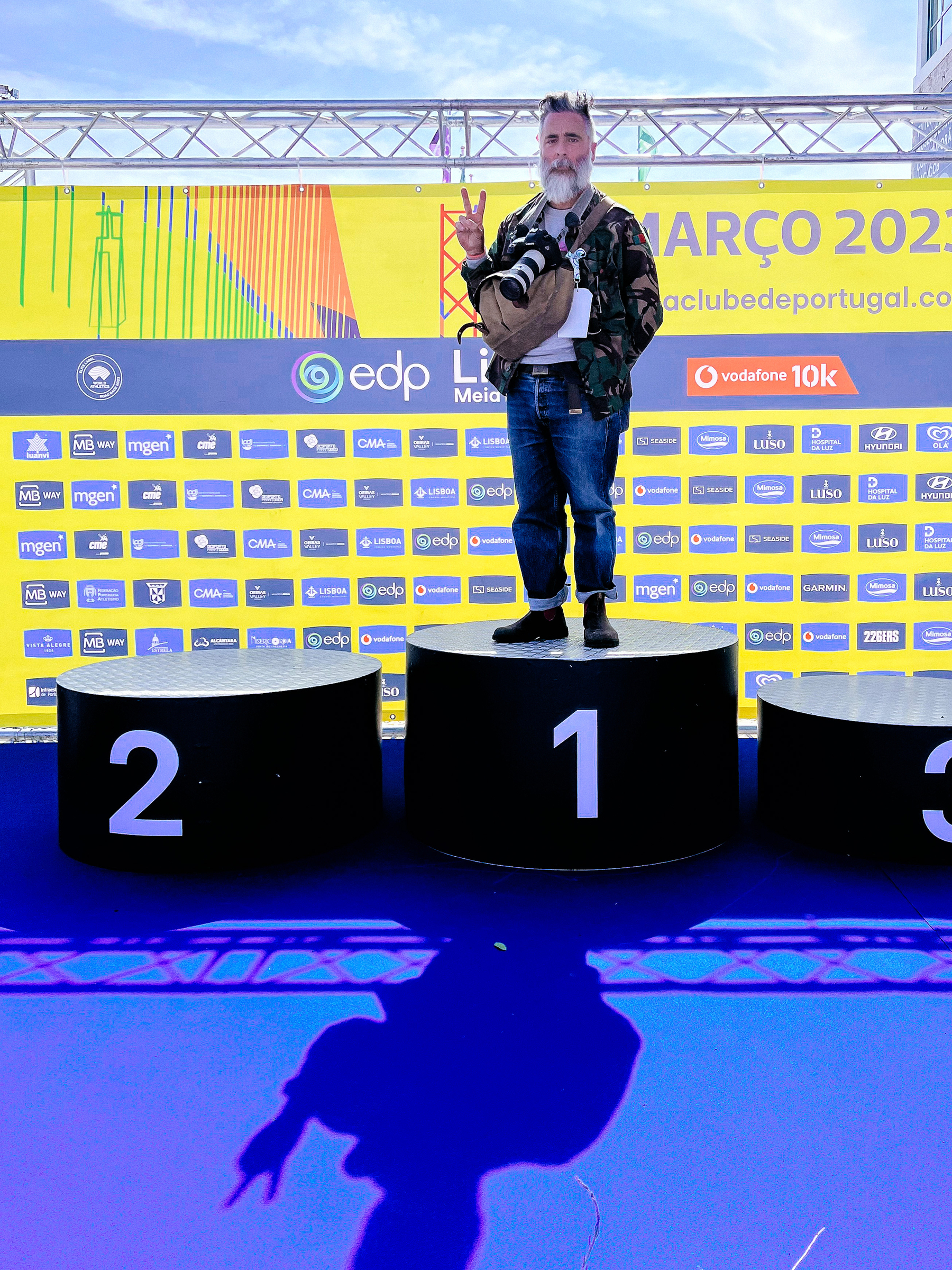 A man stands on a podium, with a camera bag. 