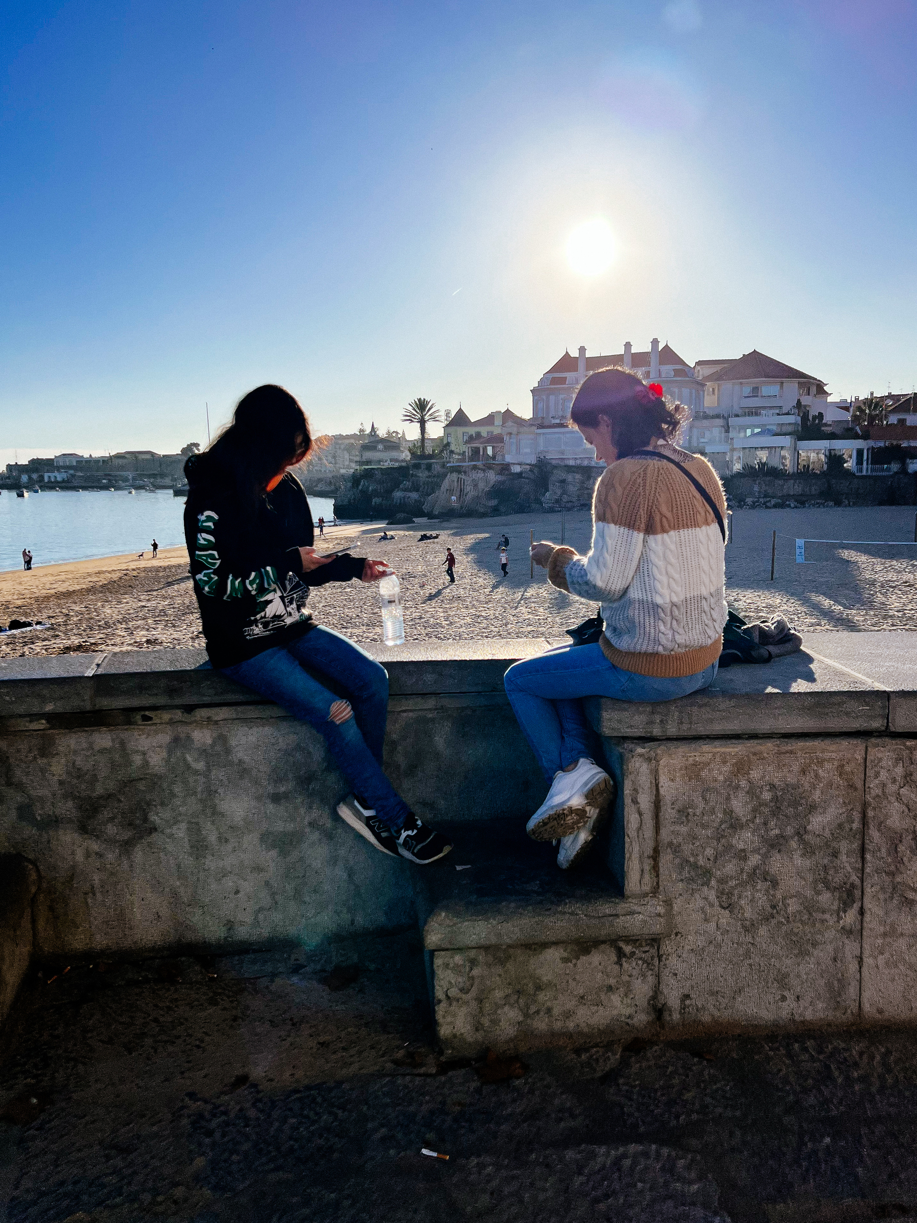 Two people sitting on a sea wall, facing away from the camera.