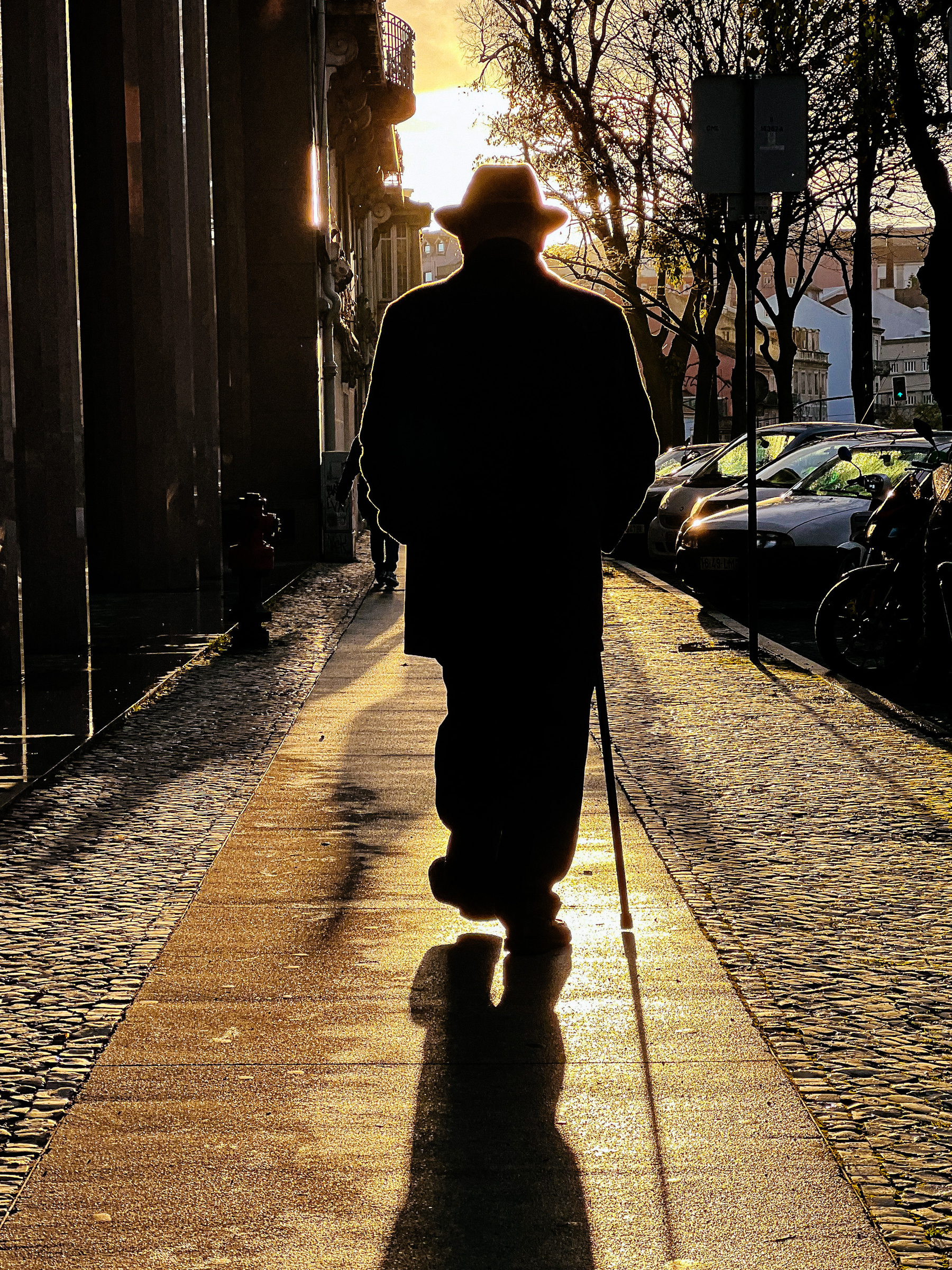 A man walking towards the sun. A cane on his right hand. 