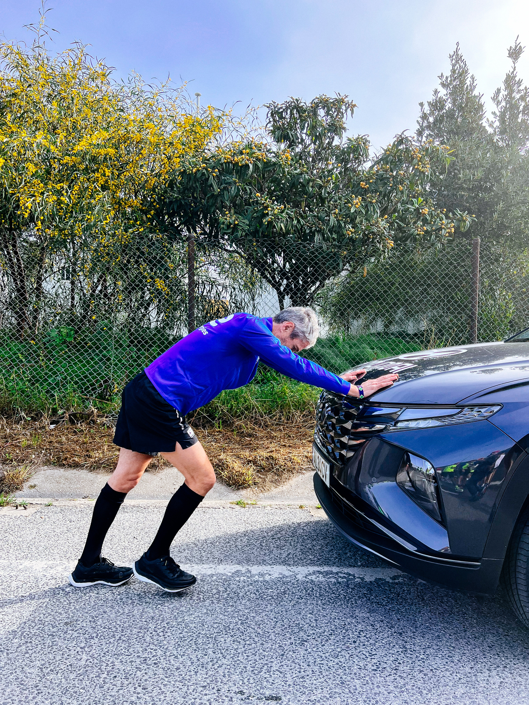 A man warms up for a run, leaning into the hood of a car 