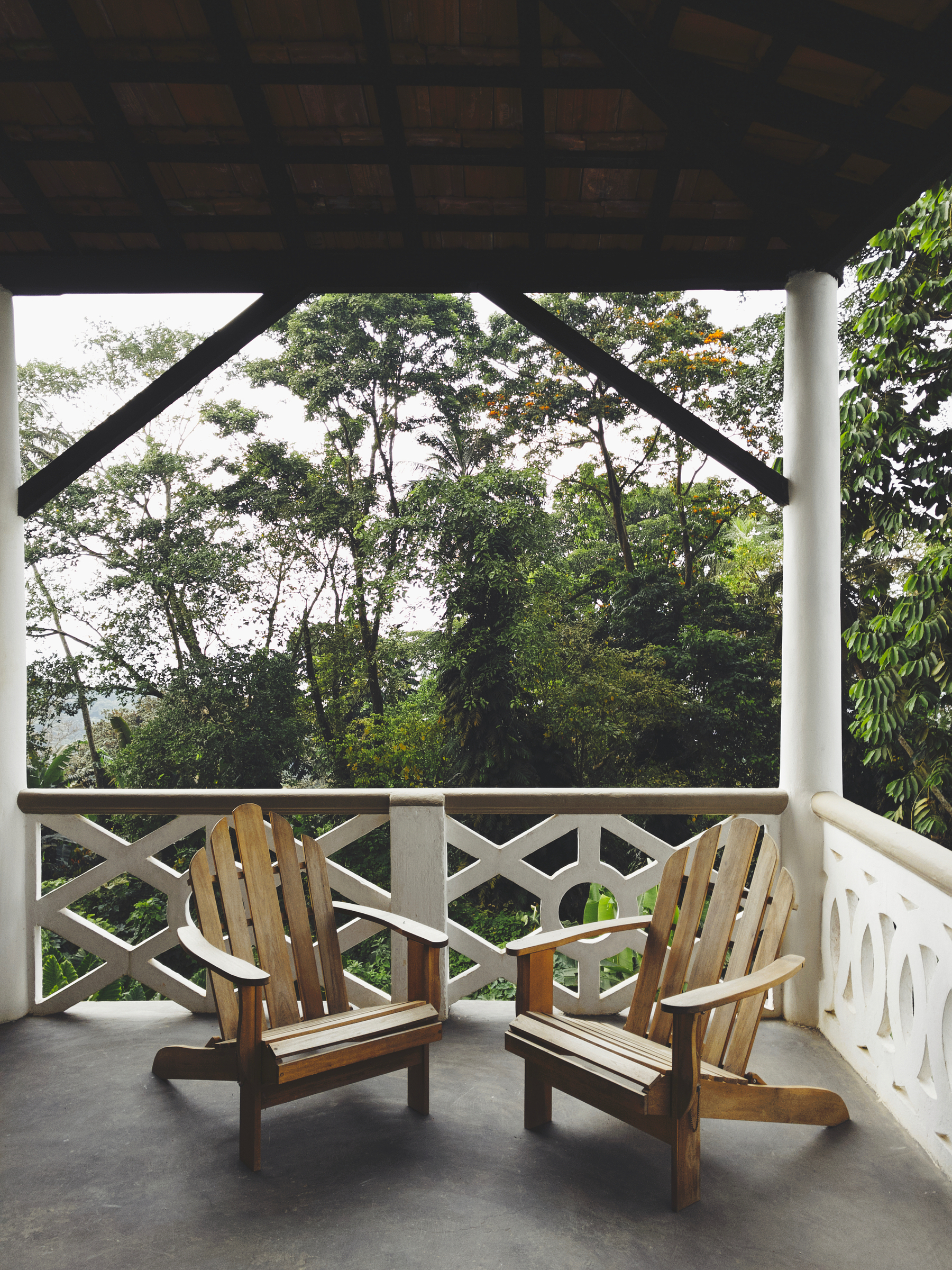 Two chairs in a balcony, with a forest in the background. 