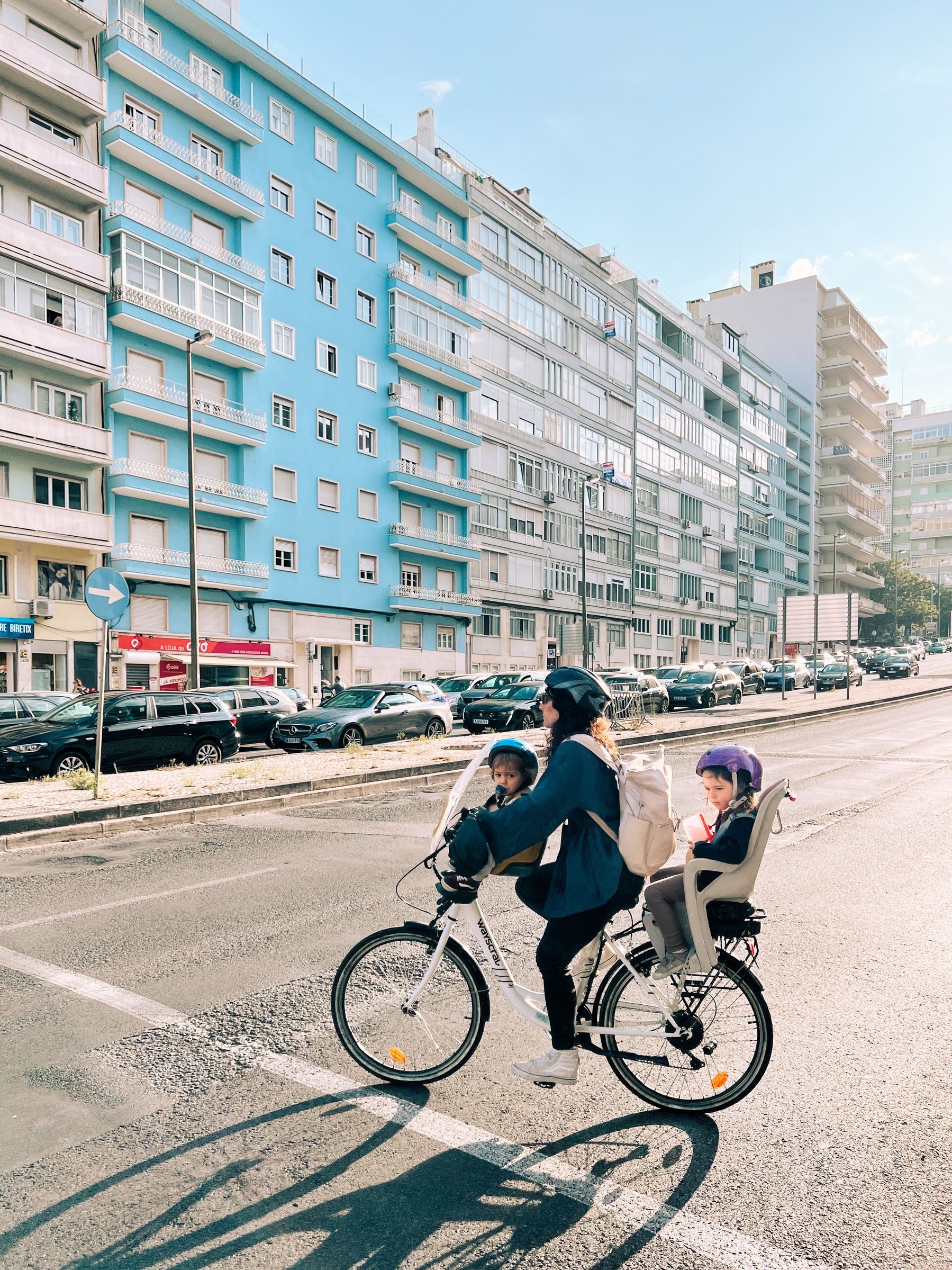 A mom and two kids ride a bicycle in the city. 