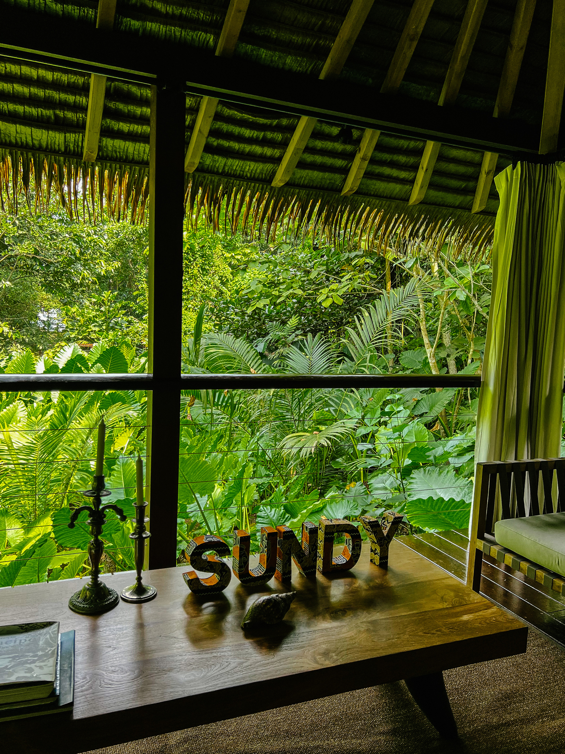 Looking out into the rainforest, we can see a table with some books, candles, and the word “Sundy” made with wooden letters. 