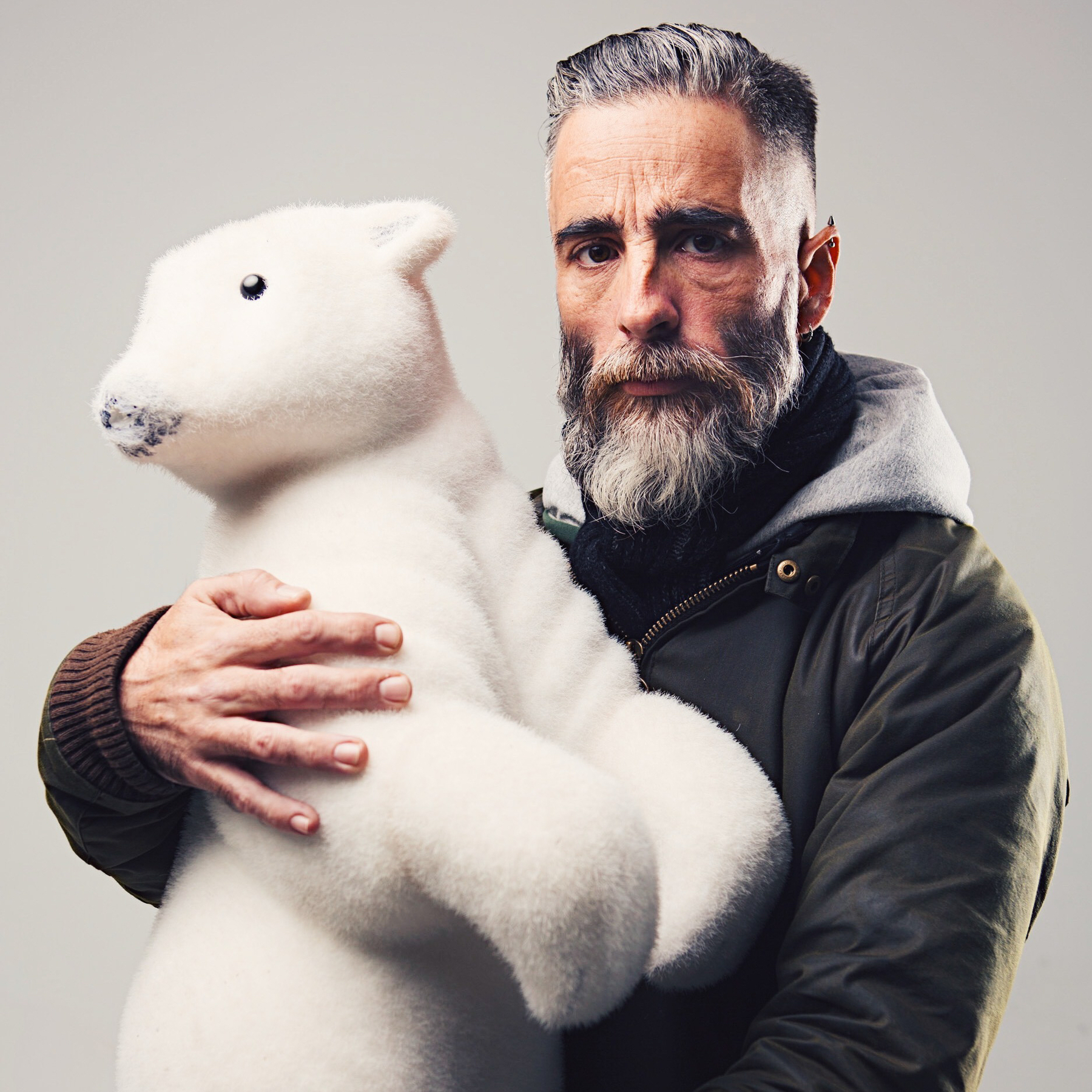 A bearded man holds a big white bear toy. 