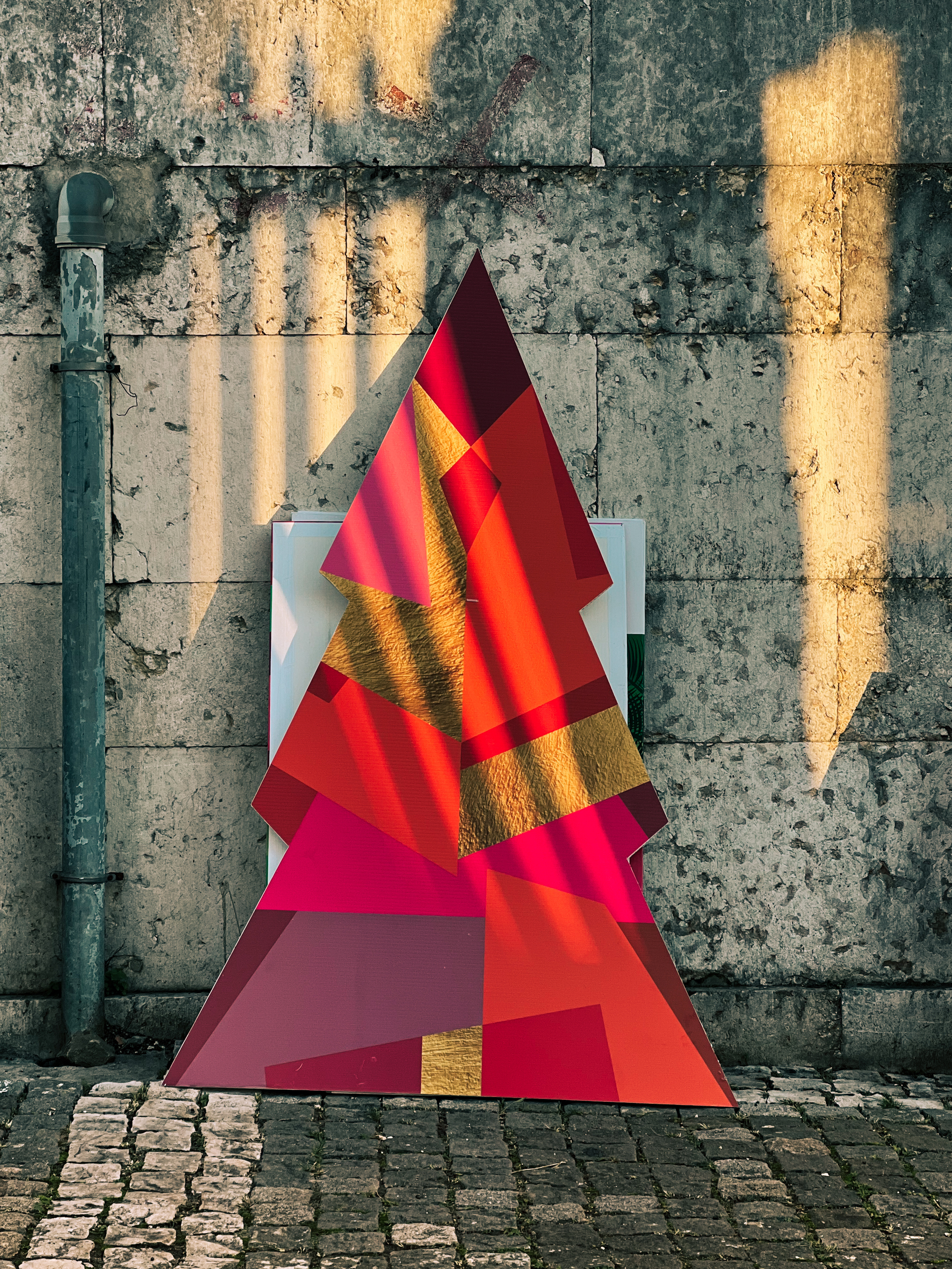 A cardboard Christmas tree, colorful, against a wall. 