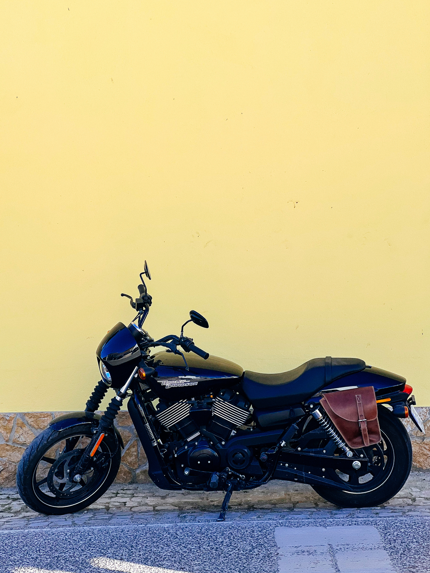 A motorcycle stands against a yellow wall. 