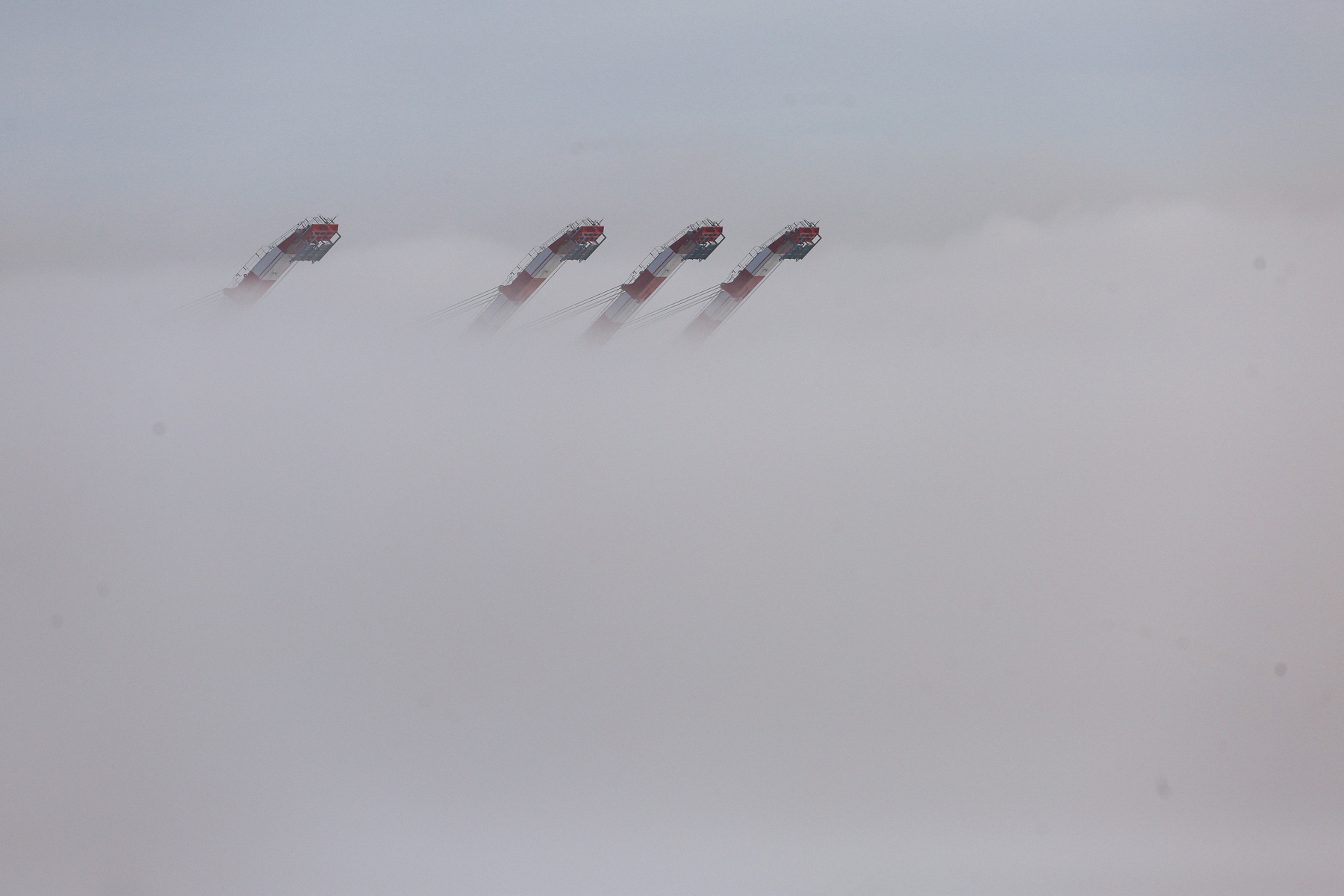 The tip of four cranes peeking out of the fog. 
