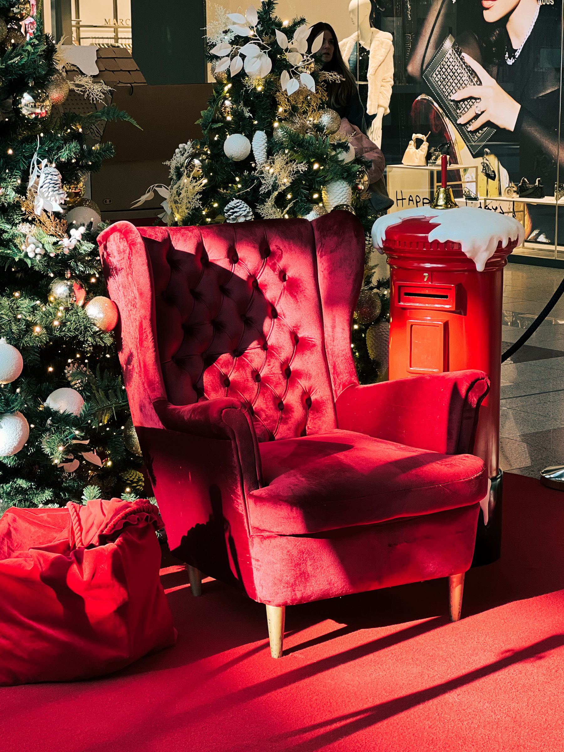 A vibrant red armchair on a red carpet, surrounded by decorated Christmas trees and a red postal box. 