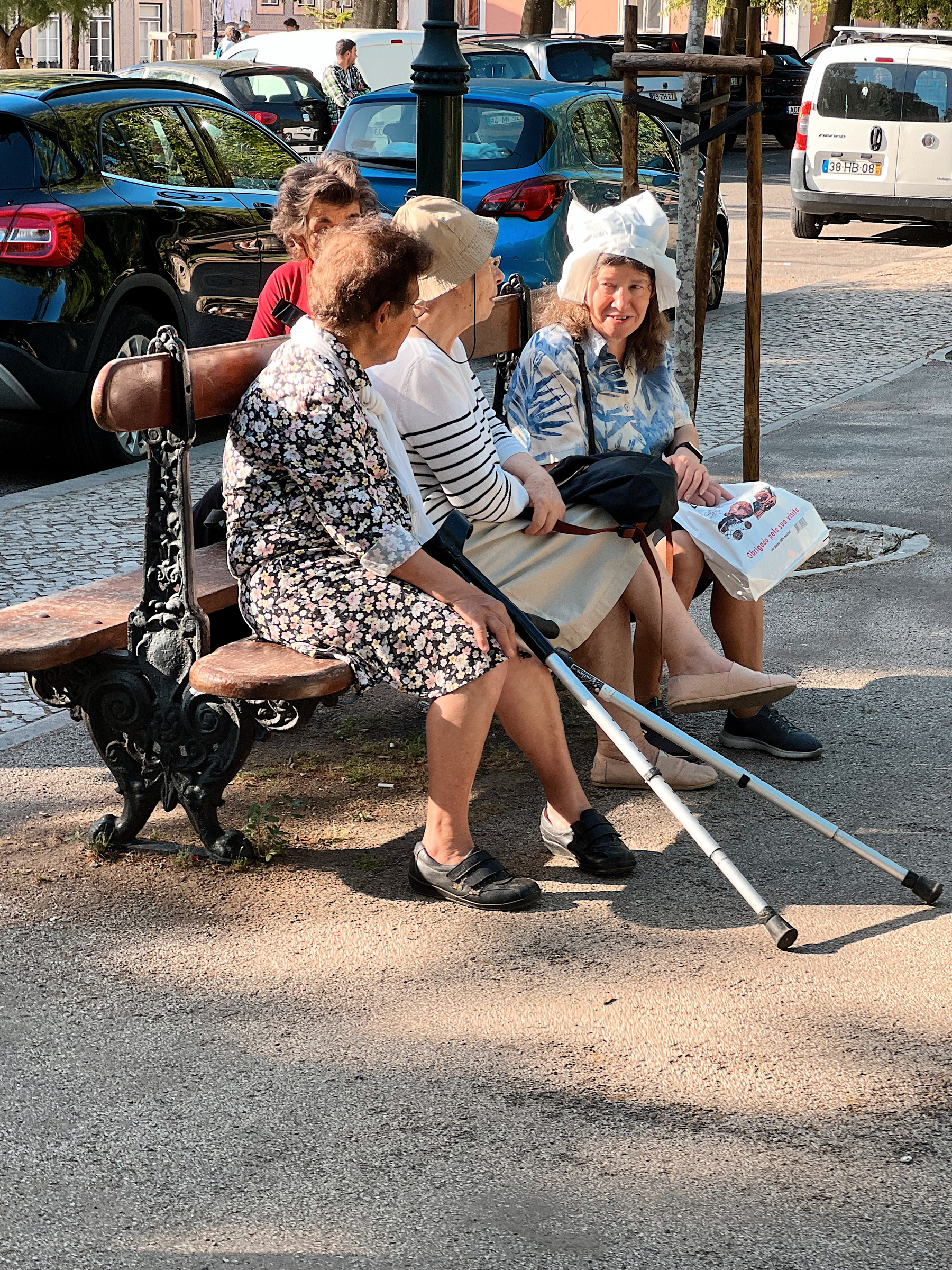 Four women talk, sitting on a bench. One of them is wearing a plastic bag over her head. 